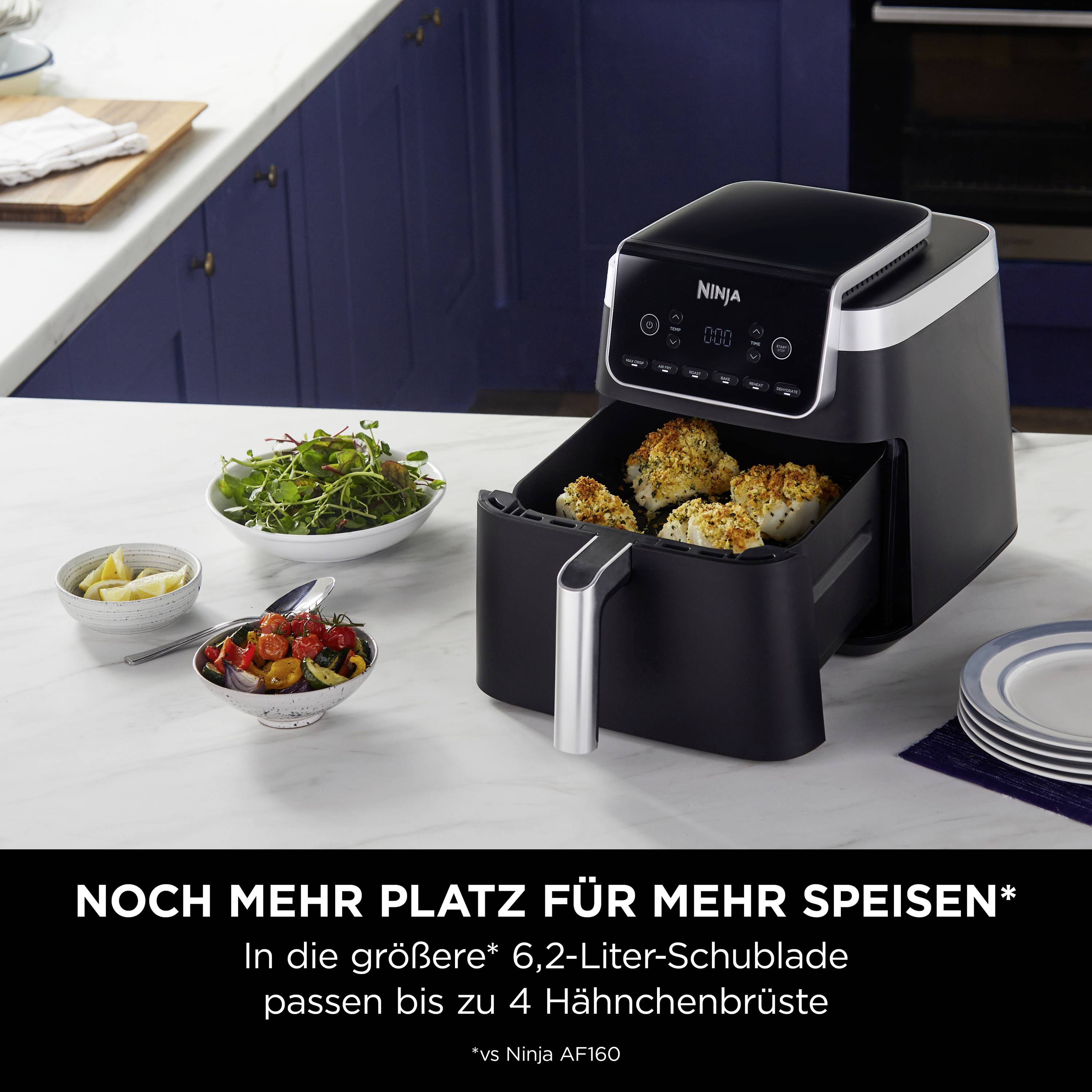 Eine schwarze Heißluftfritteuse mit geöffneter Schublade, die vier goldbraune Stücke Hähnchen enthält, steht auf einer Küchenplatte.
