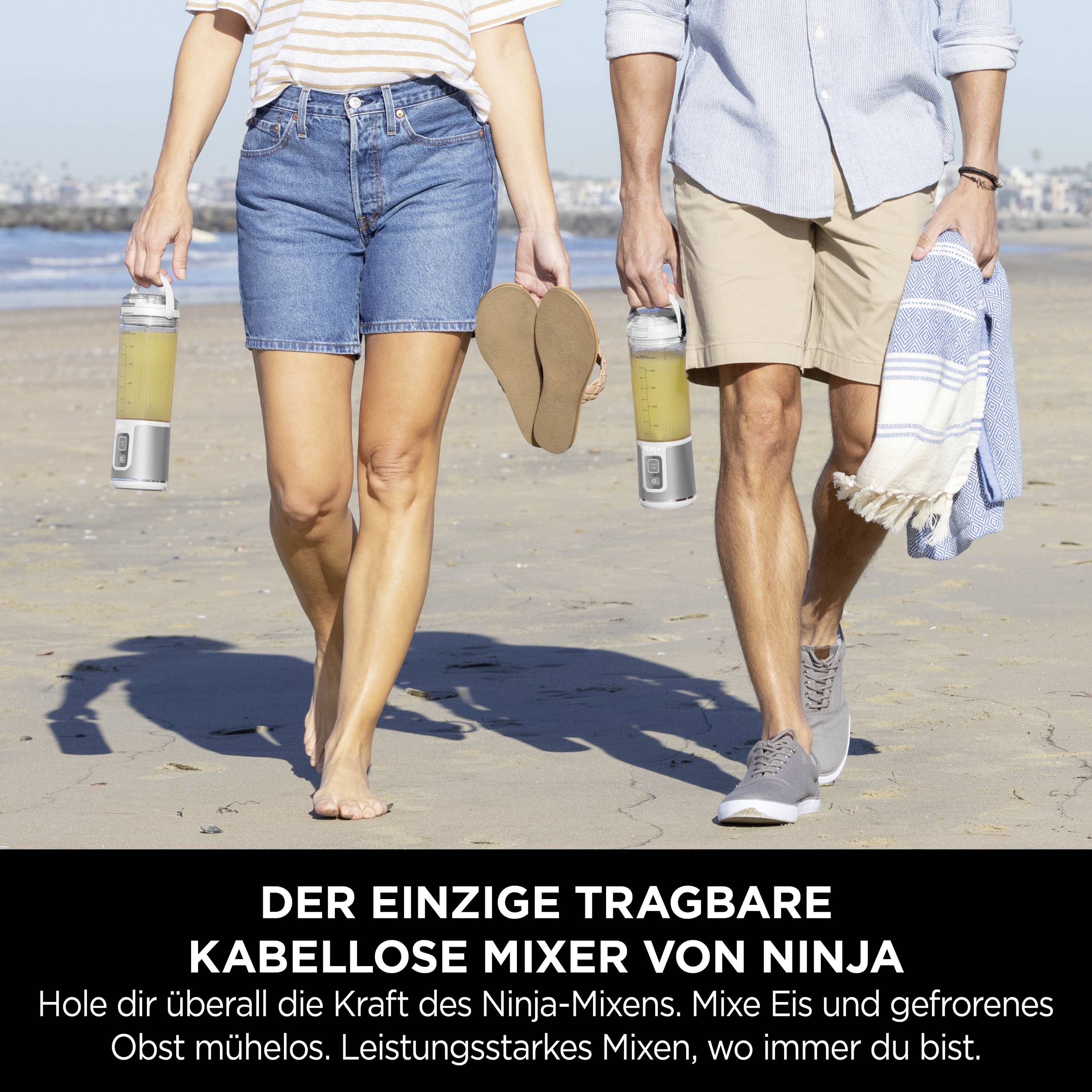 Zwei Personen gehen nebeneinander am Strand und tragen je einen tragbaren, kabellosen Mixer von Ninja. Darunter Werbetext.