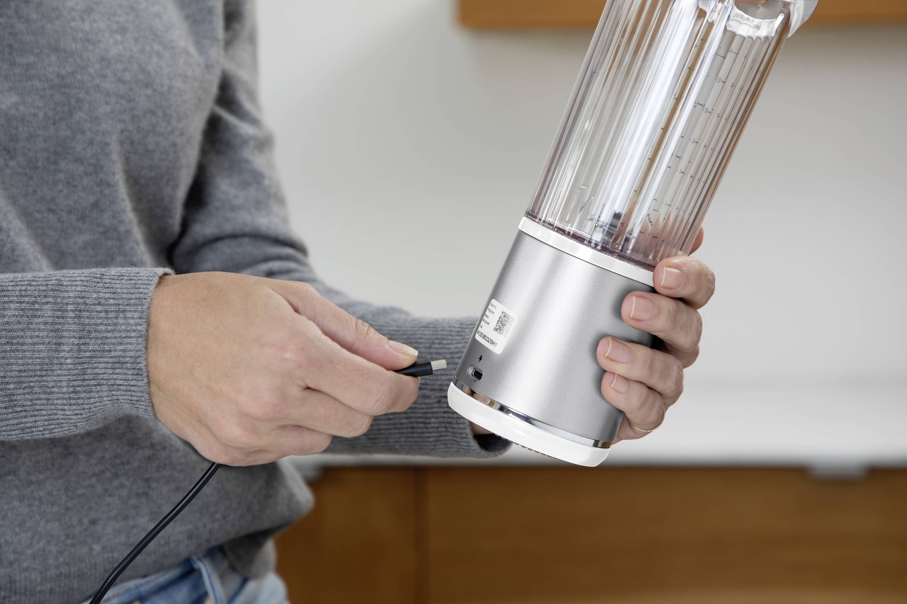 Eine Person verbindet ein Kabel mit einem tragbaren Mixer, möglicherweise zum Aufladen oder für den Betrieb.