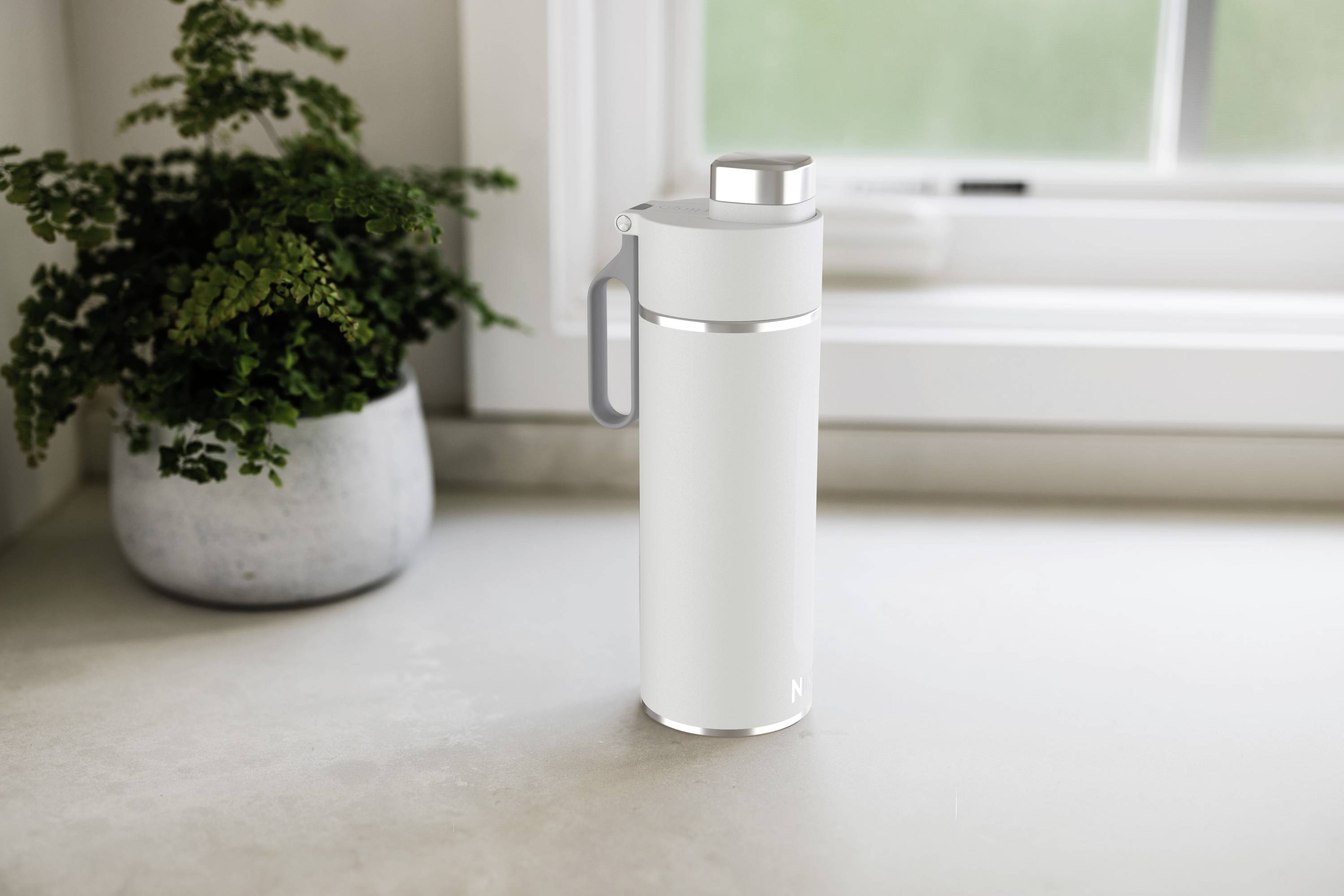 Weiße Thermosflasche auf Küchenarbeitsplatte neben Topfpflanze, mit Fenster im Hintergrund.