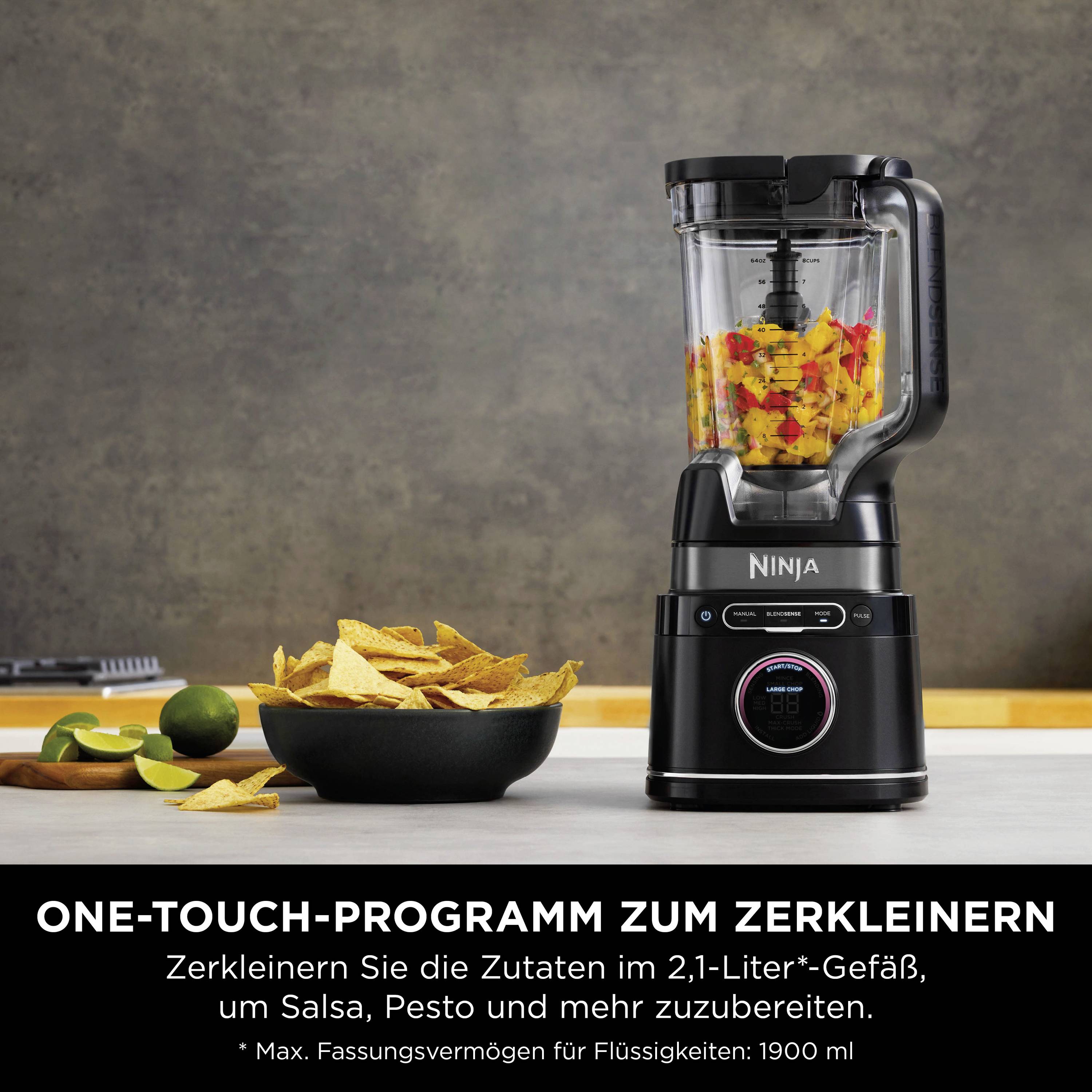 Ein Mixer mit einem Glas, gefüllt mit zerkleinerten Zutaten steht auf einer Arbeitsplatte. Daneben Schalen mit Chips und Limetten.