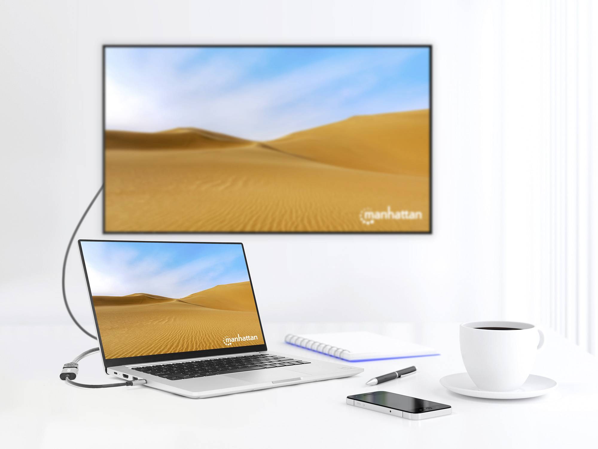Laptop verbunden mit Bildschirm, beide zeigen Wüstenlandschaft. Daneben ein Notizbuch, Kugelschreiber, Smartphone und Kaffeetasse.