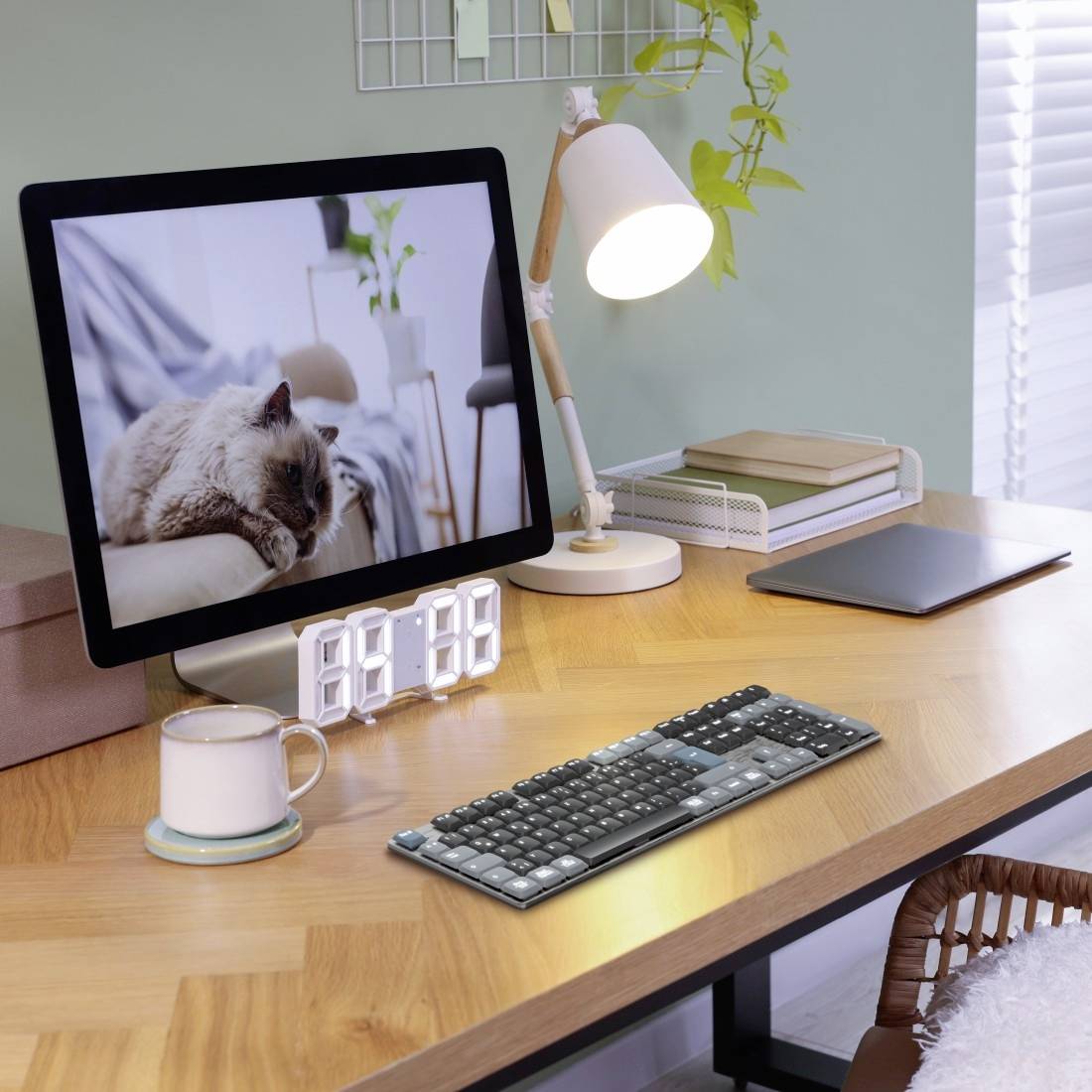 Ein moderner Schreibtisch mit Holzoberfläche, darauf ein Computerbildschirm mit einem schlafenden Tier, eine Lampe, Tastatur und Tasse.