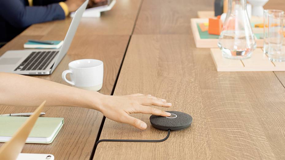 Eine Person aktiviert ein Konferenzmikrofon auf einem Tisch mit Laptop und Notizbuch, bereit für ein Meeting.