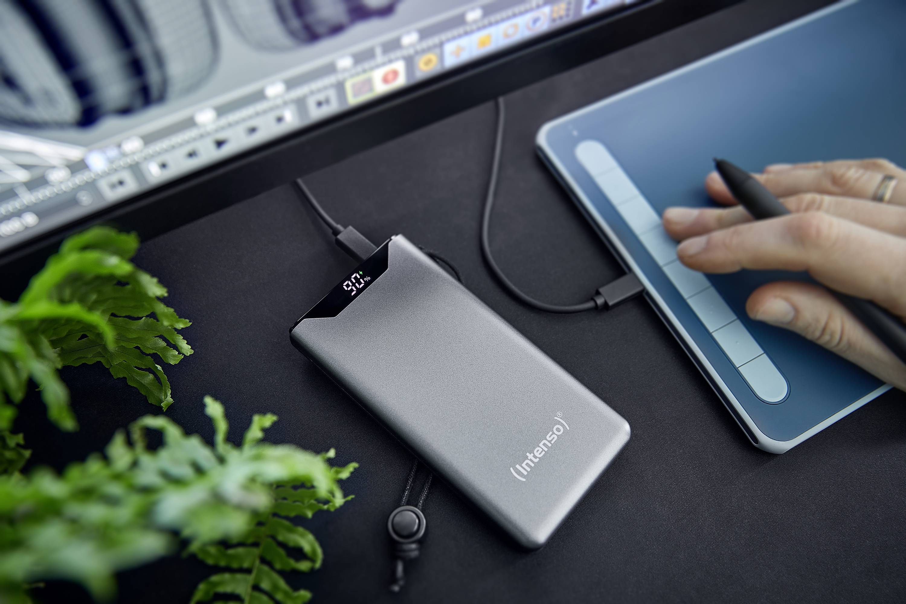 Ein tragbarer externer SSD-Speicher in der Nähe eines Grafiktabletts wird angeschlossen, während auf einem Bildschirm grafische Software läuft.
