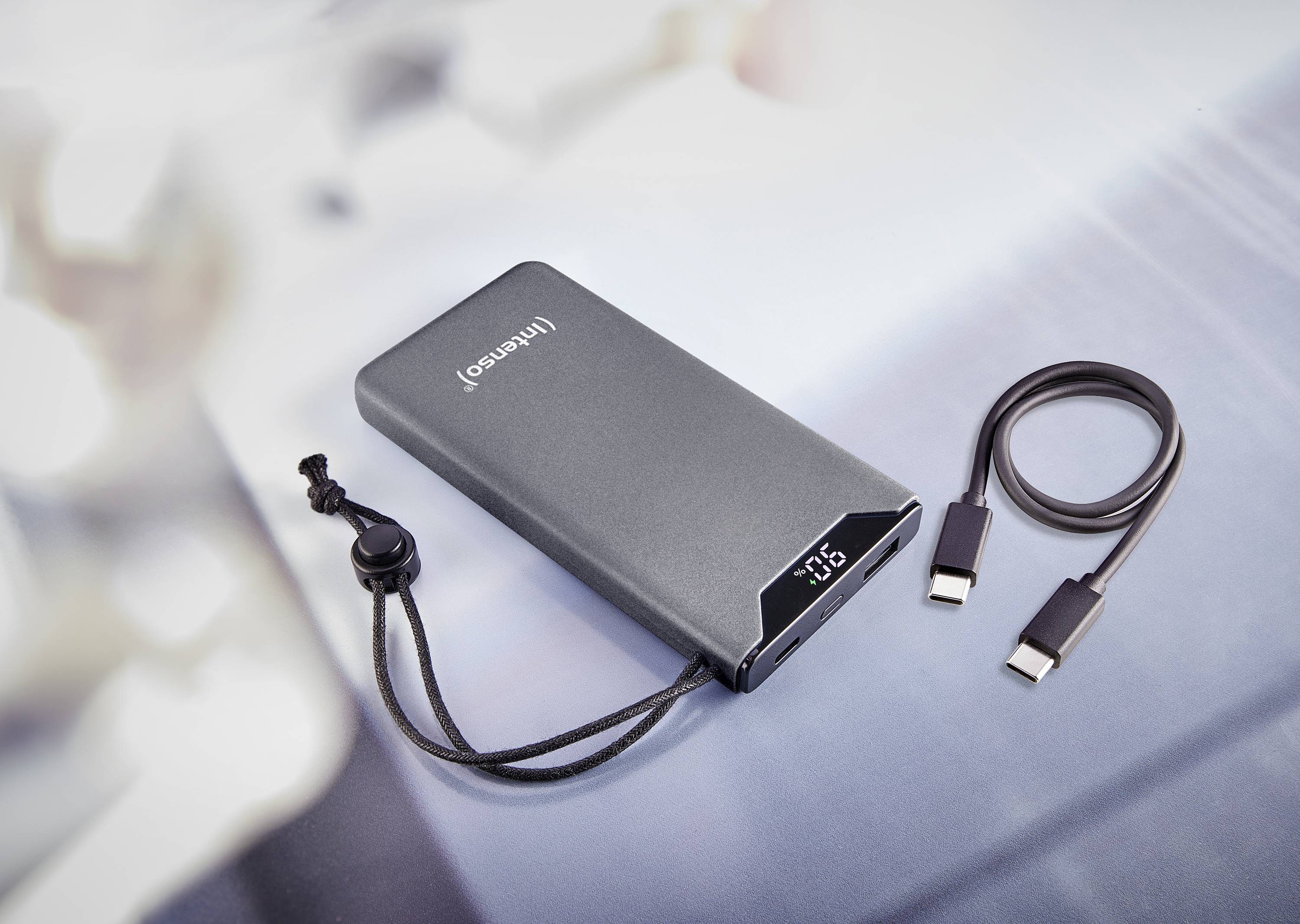 Eine tragbare Powerbank mit LED-Anzeige und Kabel, die auf einem Tisch liegt. Die Kapazität wird auf dem Display angezeigt.