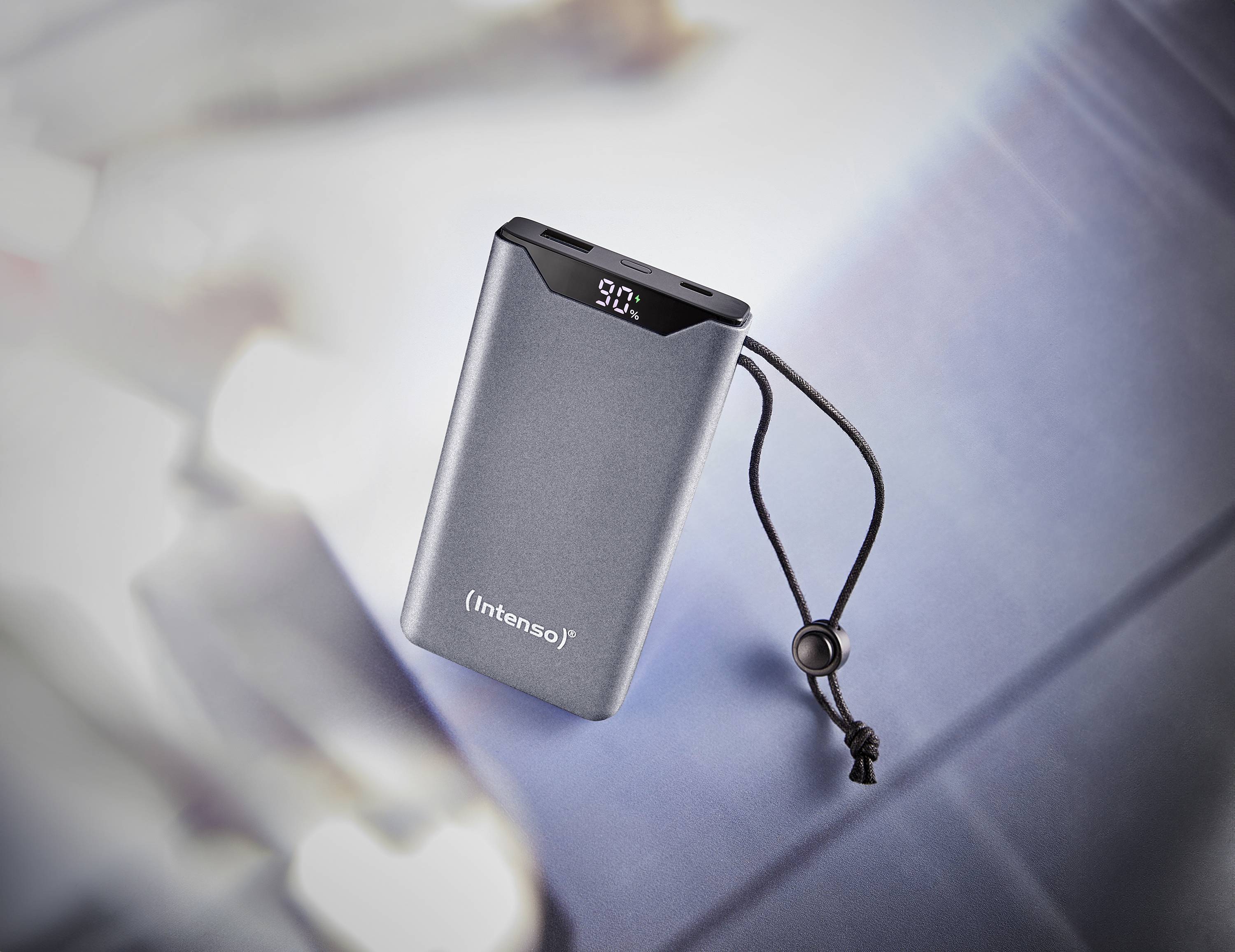 Tragbare Powerbank mit Digitalanzeige auf einem unscharfen, blauen Hintergrund. Zeigt '90%' an. Geeignet für unterwegs.
