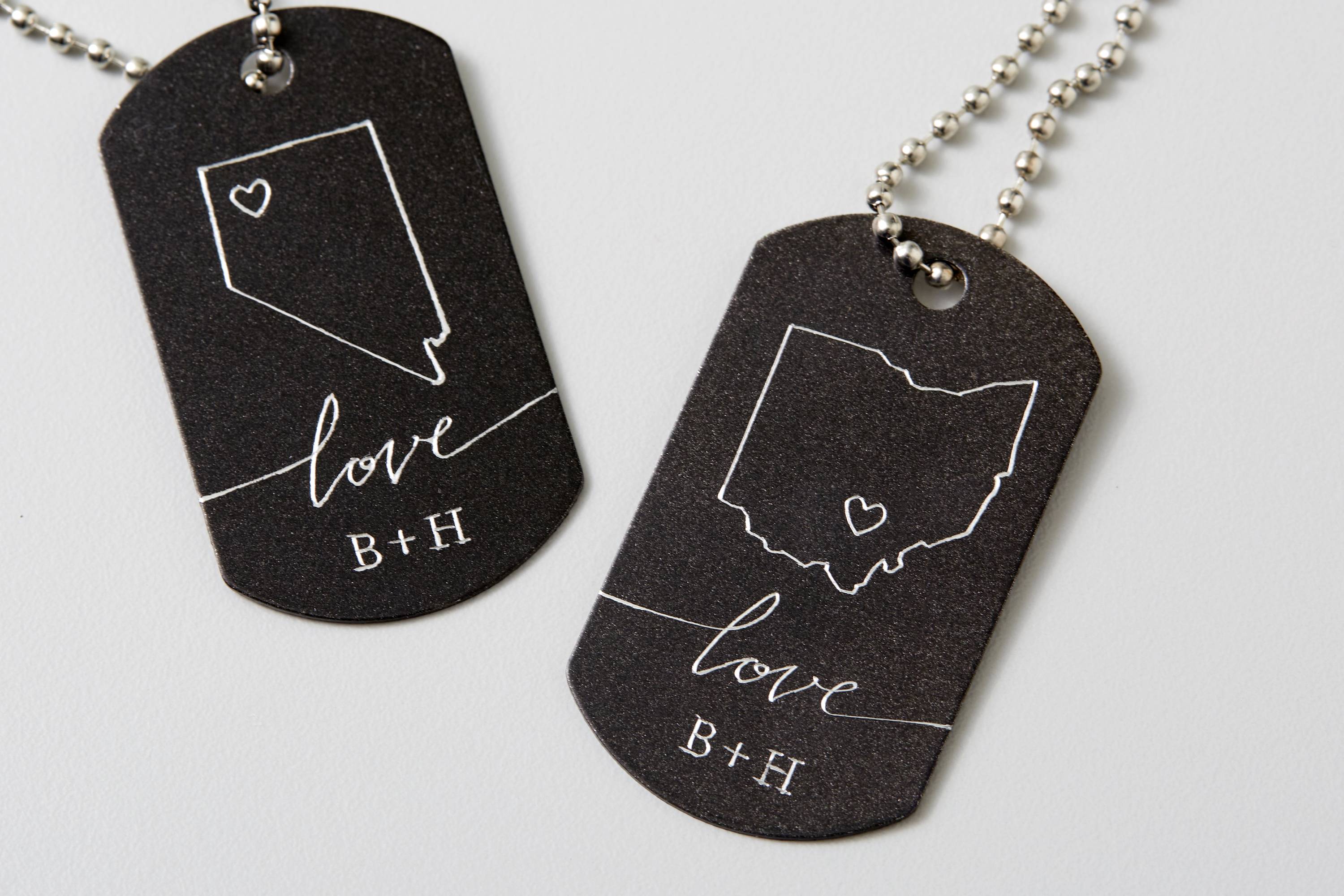 Zwei schwarze Halsketten-Anhänger mit den Umrissen von Nevada und Ohio, jeweils mit einem Herzsymbol und dem Wort 'love B+H'.