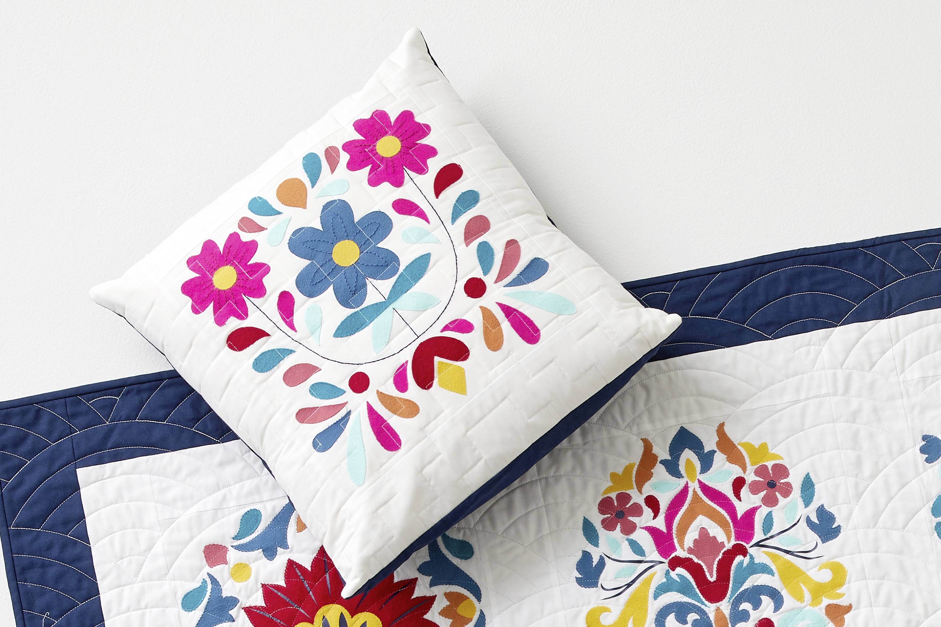 Ein Kissen mit buntem Blumenmuster liegt auf einer passenden Bettdecke, die ebenfalls mit floralen Motiven verziert ist.