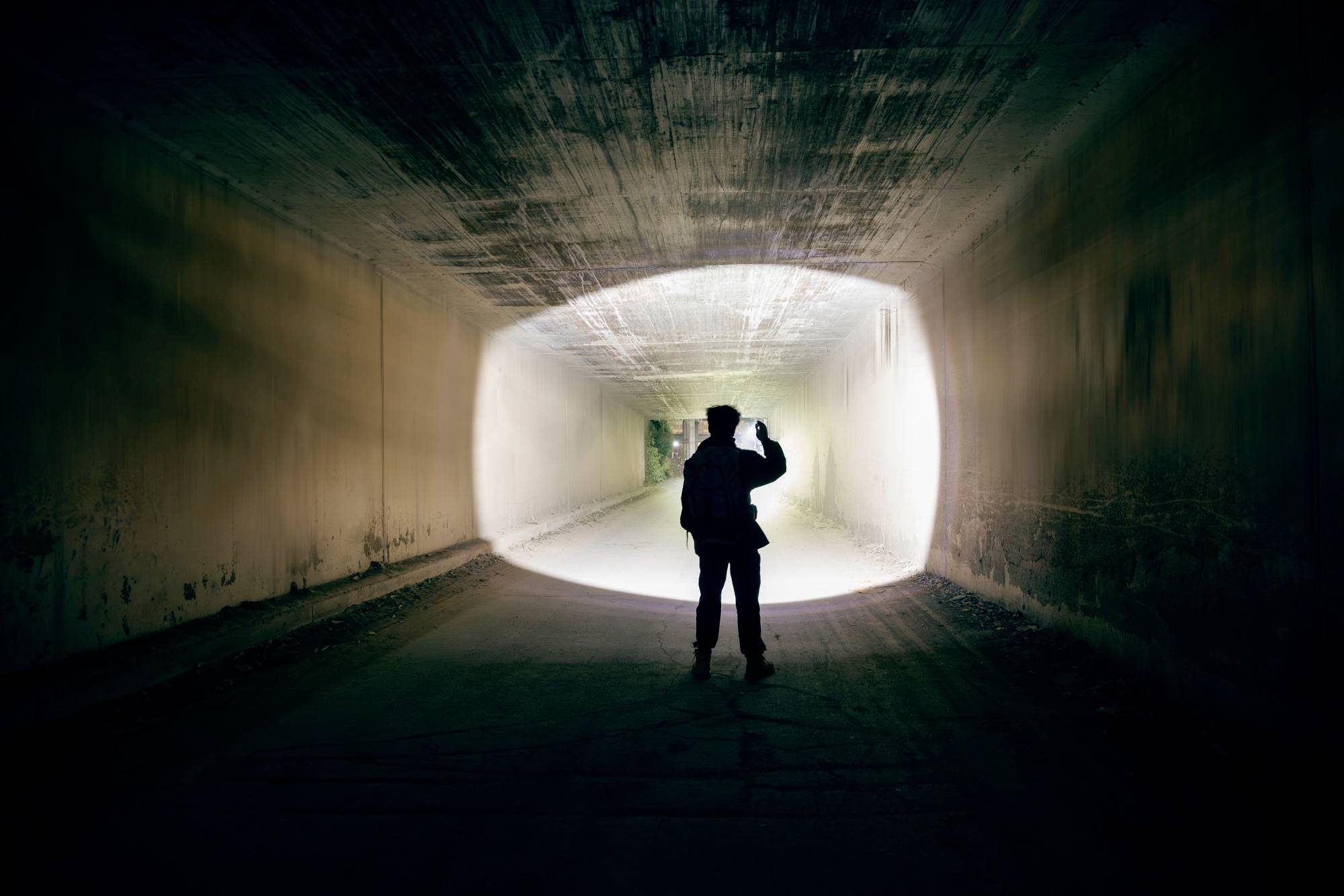Eine Person steht in einem beleuchteten Tunnel und schaut nach draußen. Silhouette vor hellem Ausgang.