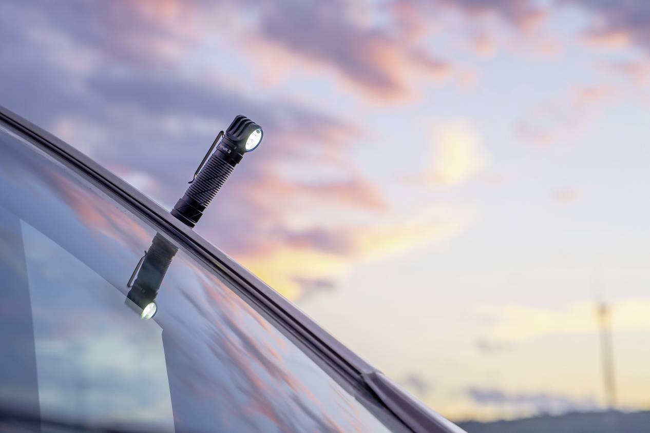 Taschenlampe auf Autodach bei Sonnenuntergang, mit pastellfarbenem Himmel im Hintergrund, der sanfte Abendstimmung erzeugt.