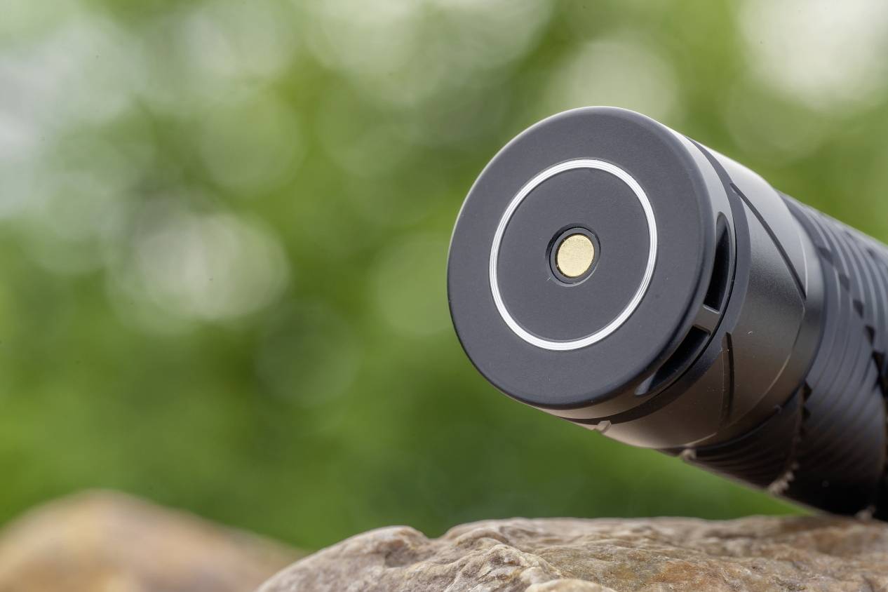 Taschenlampe liegt auf einem Felsen in einem grünen, verschwommenen Hintergrund. Der Fokus liegt auf dem vorderen Ende der Taschenlampe.