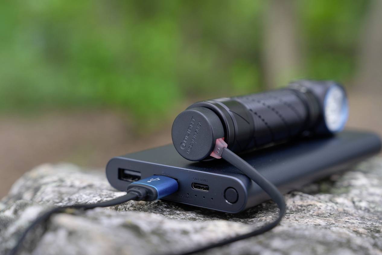 Auf einem Stein liegende Powerbank mit einer angeschlossenen Taschenlampe, umgeben von unscharfem, grünem Hintergrund.