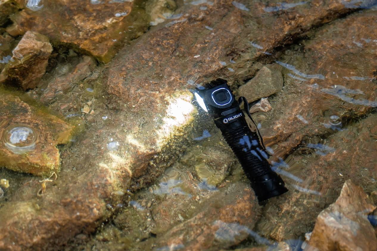 Taschenlampe im flachen Wasser auf Felsen liegend, die still leuchtet und die umgebenden Steine leicht erhellt.
