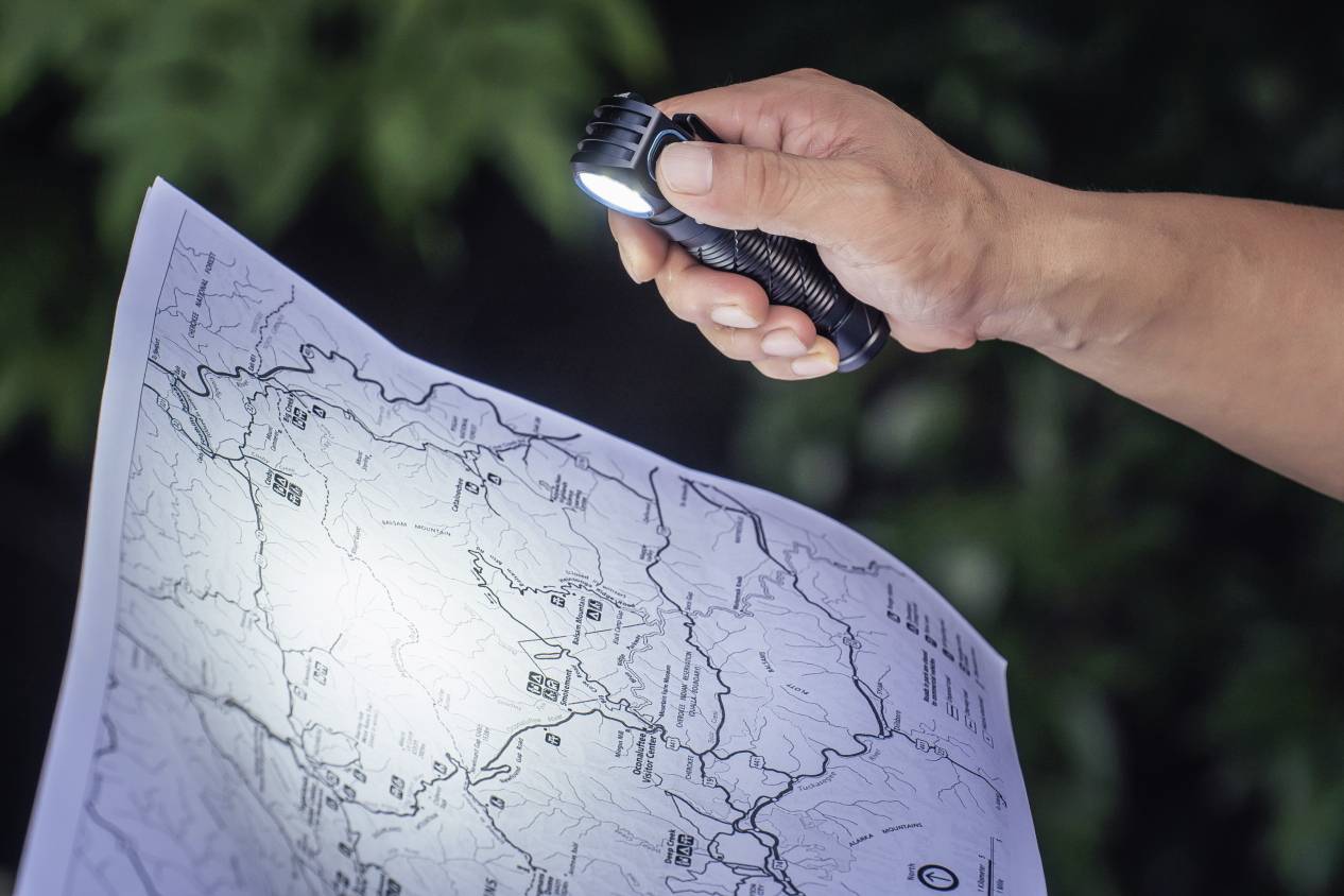Eine Person beleuchtet mit einer Taschenlampe eine detaillierte Karte. Die Karte zeigt geografische Linien und Orte.