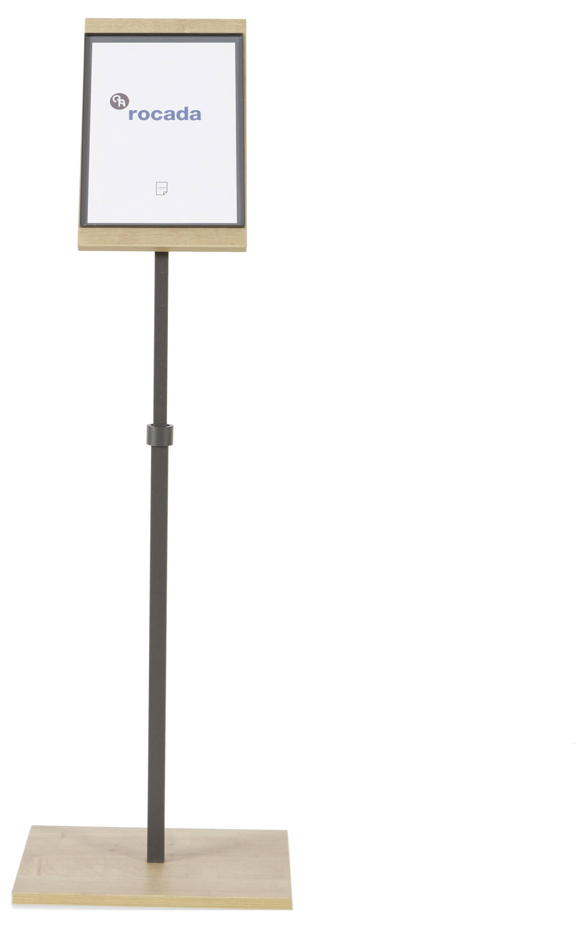 Ein Holzständer mit einem Bildschirm zeigt das Logo 'rocada'. Der Ständer ist aufrecht und schlicht gestaltet.