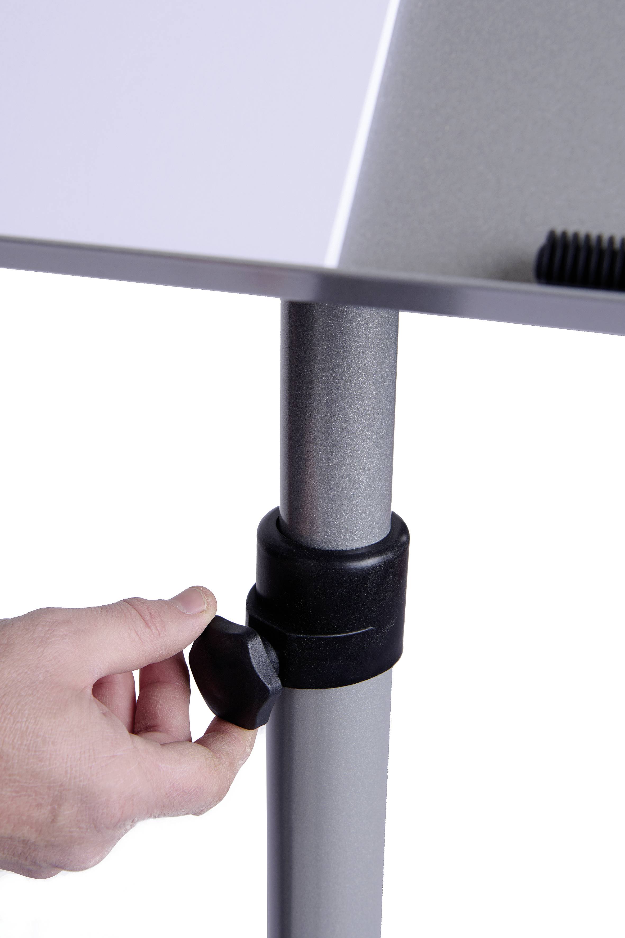 Eine Hand dreht einen schwarzen Knopf, um die Höhe eines silbernen Tischbeins einzustellen.