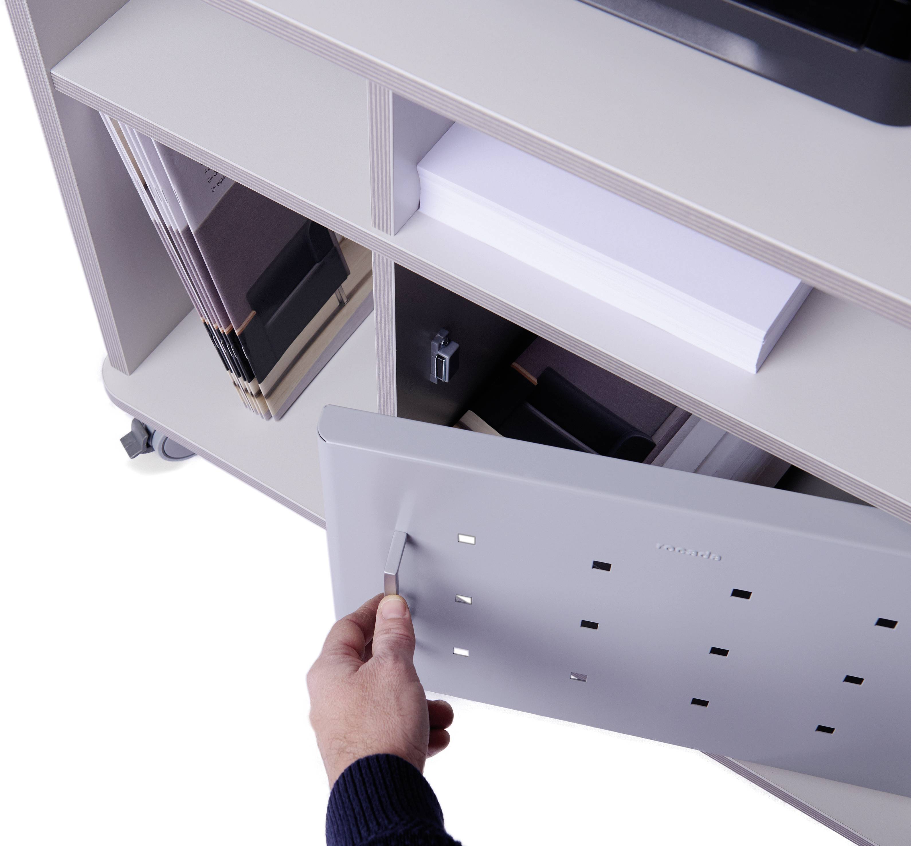 Hand öffnet weiße Schublade eines Rollcontainers. Im Fach liegen Aktenordner und Büroklammern.