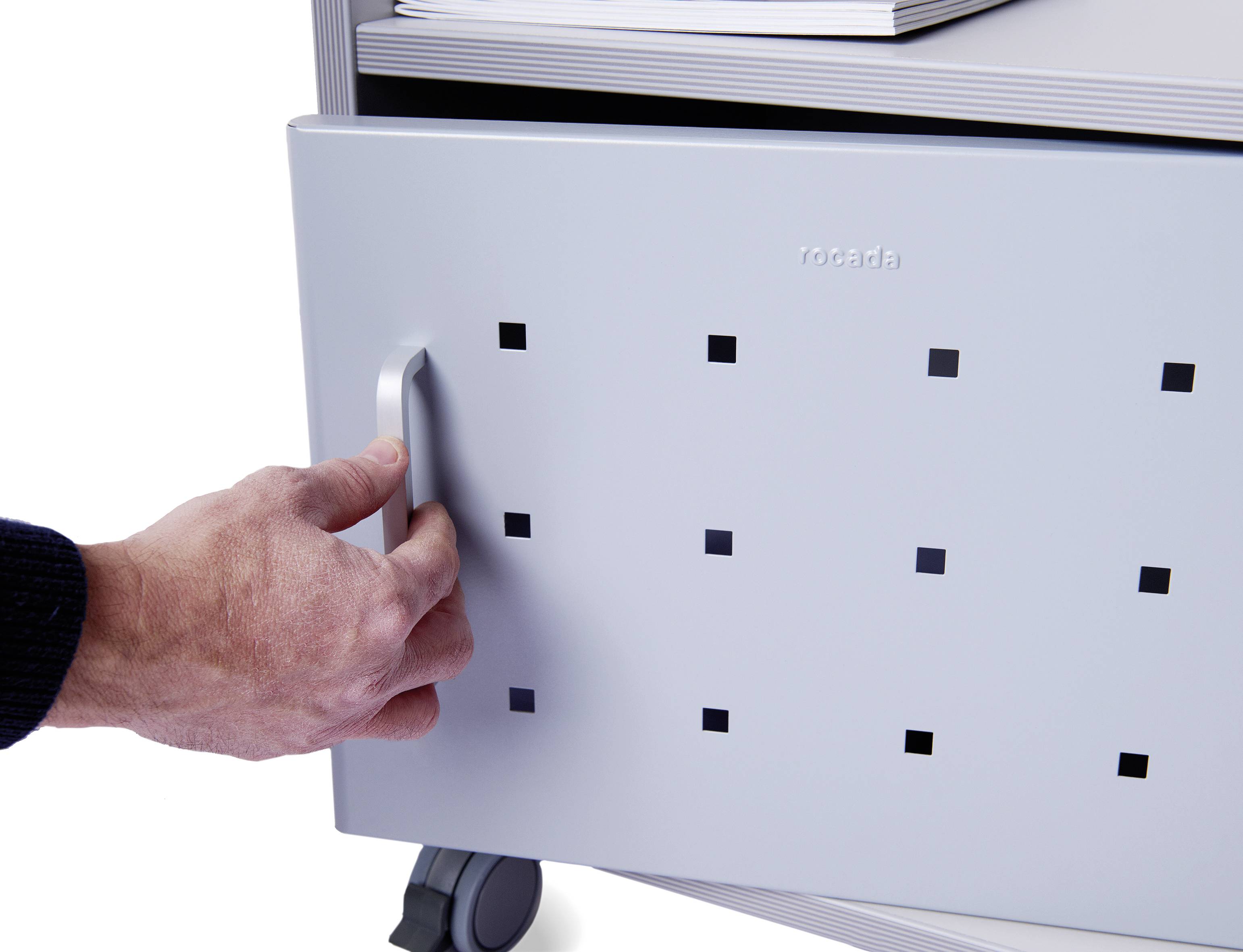 Eine Hand öffnet eine graue Schublade mit quadratischen Löchern an einem mobilen Möbelsystem.