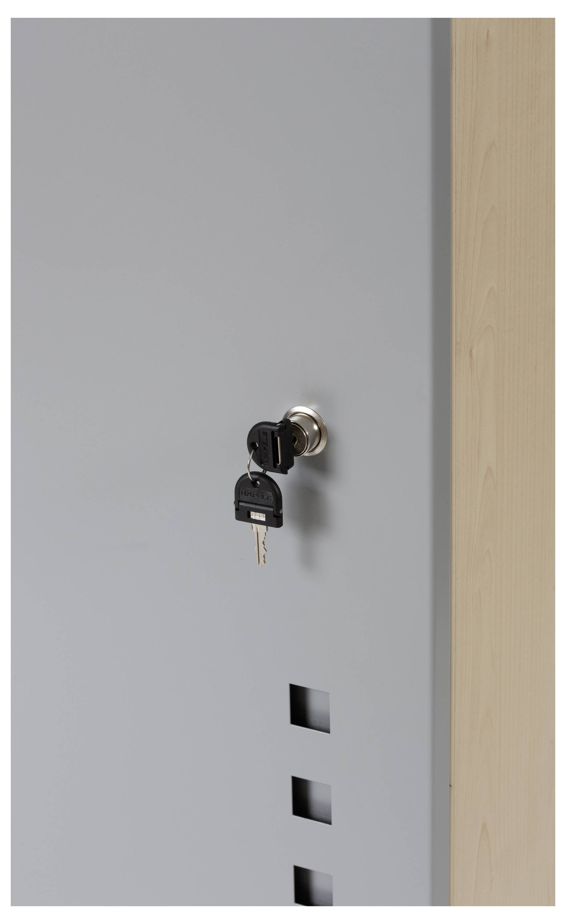 Ein grauer Aktenschrank mit einem Metallschloss, in dem zwei Schlüssel stecken. Daneben eine Holzpaneele.