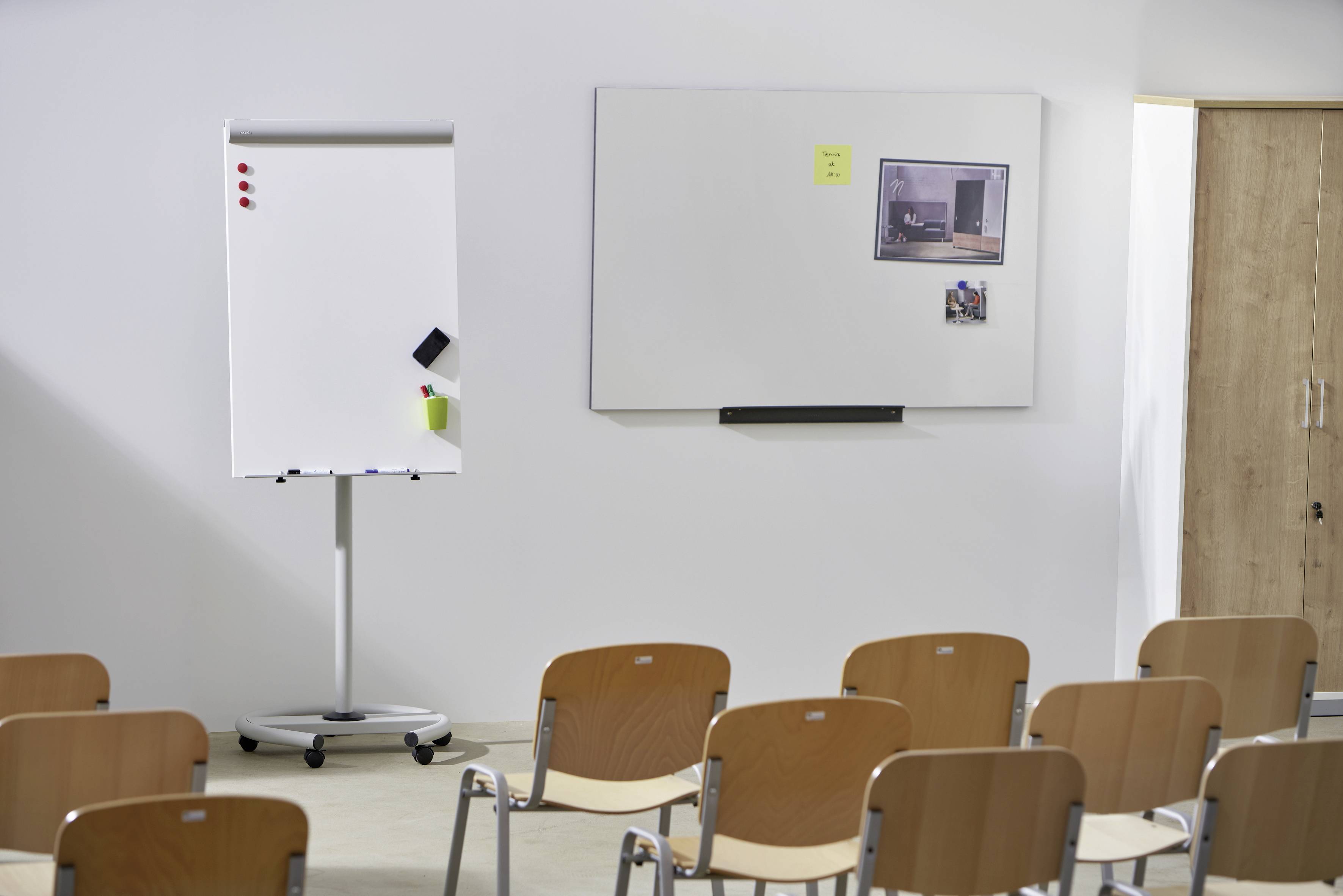 Mehrere Stuhlreihen vor einem weißen Flipchart und einer Wandtafel in einem Veranstaltungsraum.