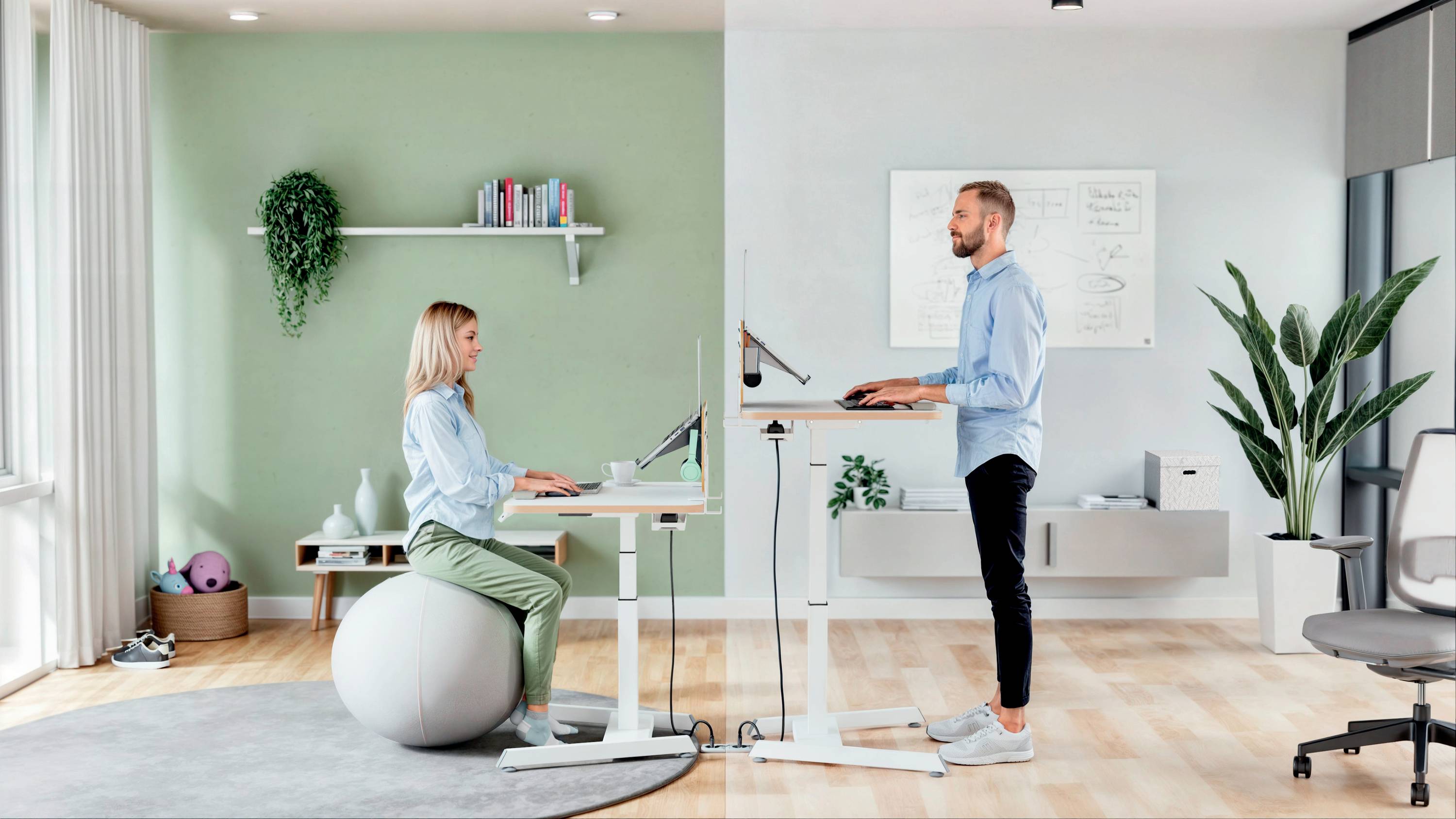 Eine Frau und ein Mann arbeiten in einem ergonomischen Büro. Sie sitzt auf einem Gymnastikball, er steht an einem höhenverstellbaren Schreibtisch.