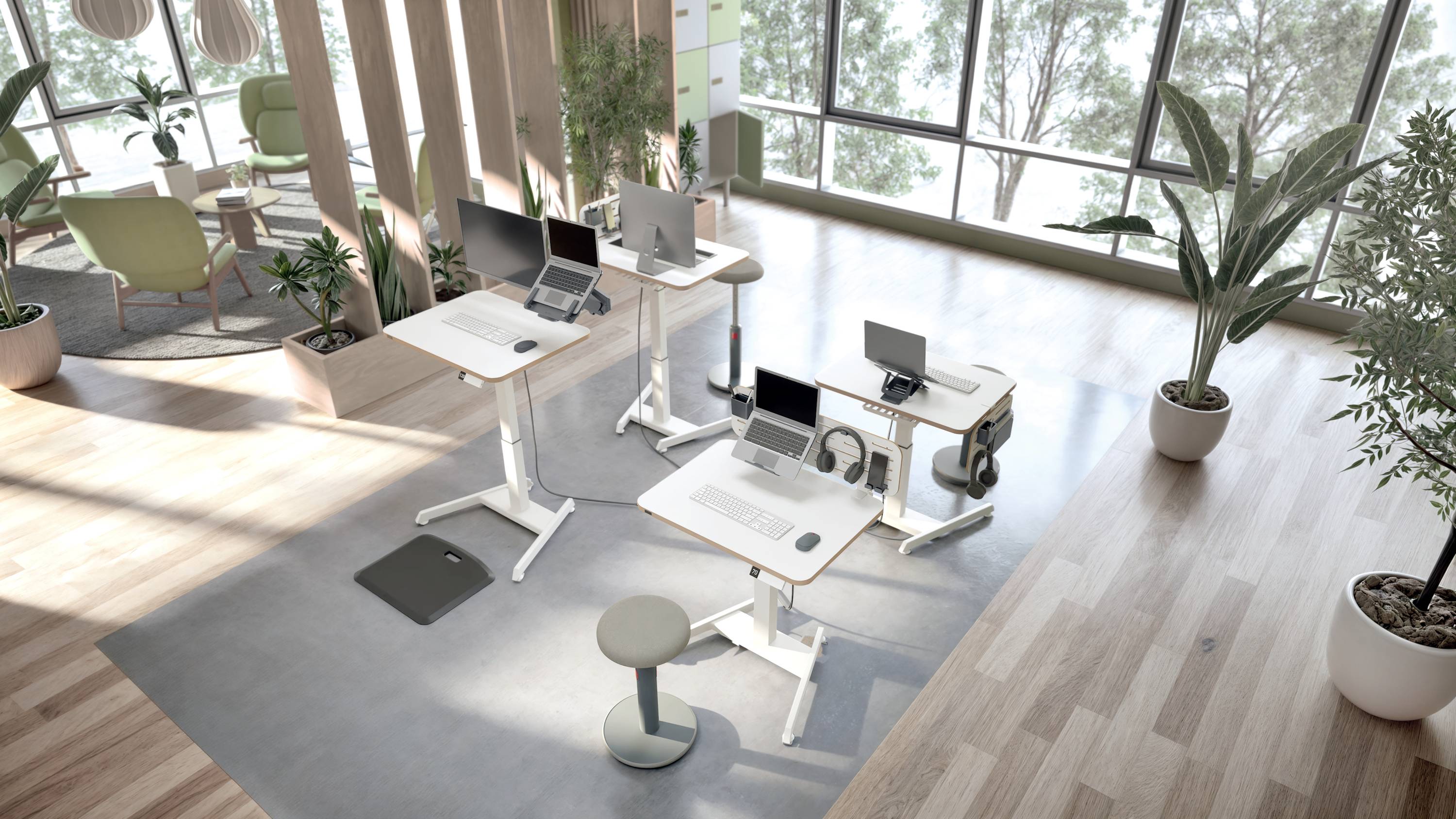 Moderne Büroumgebung mit höhenverstellbaren Schreibtischen und Laptops, umgeben von großen Fenstern und Pflanzen, die eine helle Atmosphäre schaffen.