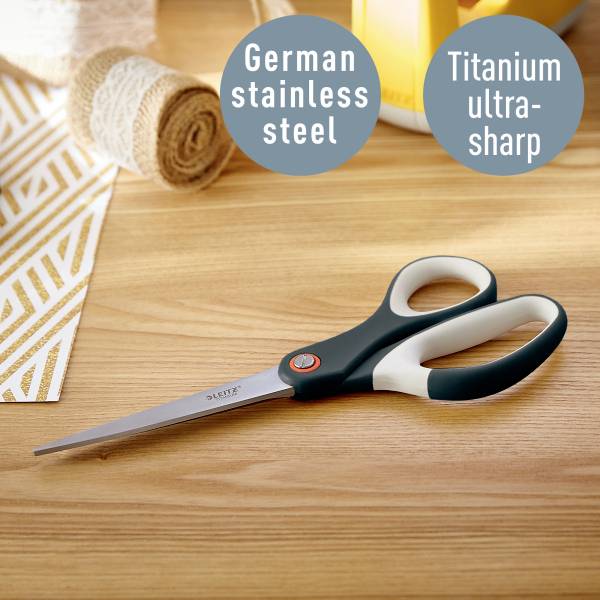 Eine Schere liegt auf einem Tisch mit Stoffrollen. Beschriftungen weisen auf deutschen Edelstahl und ultrascharfes Titan hin.