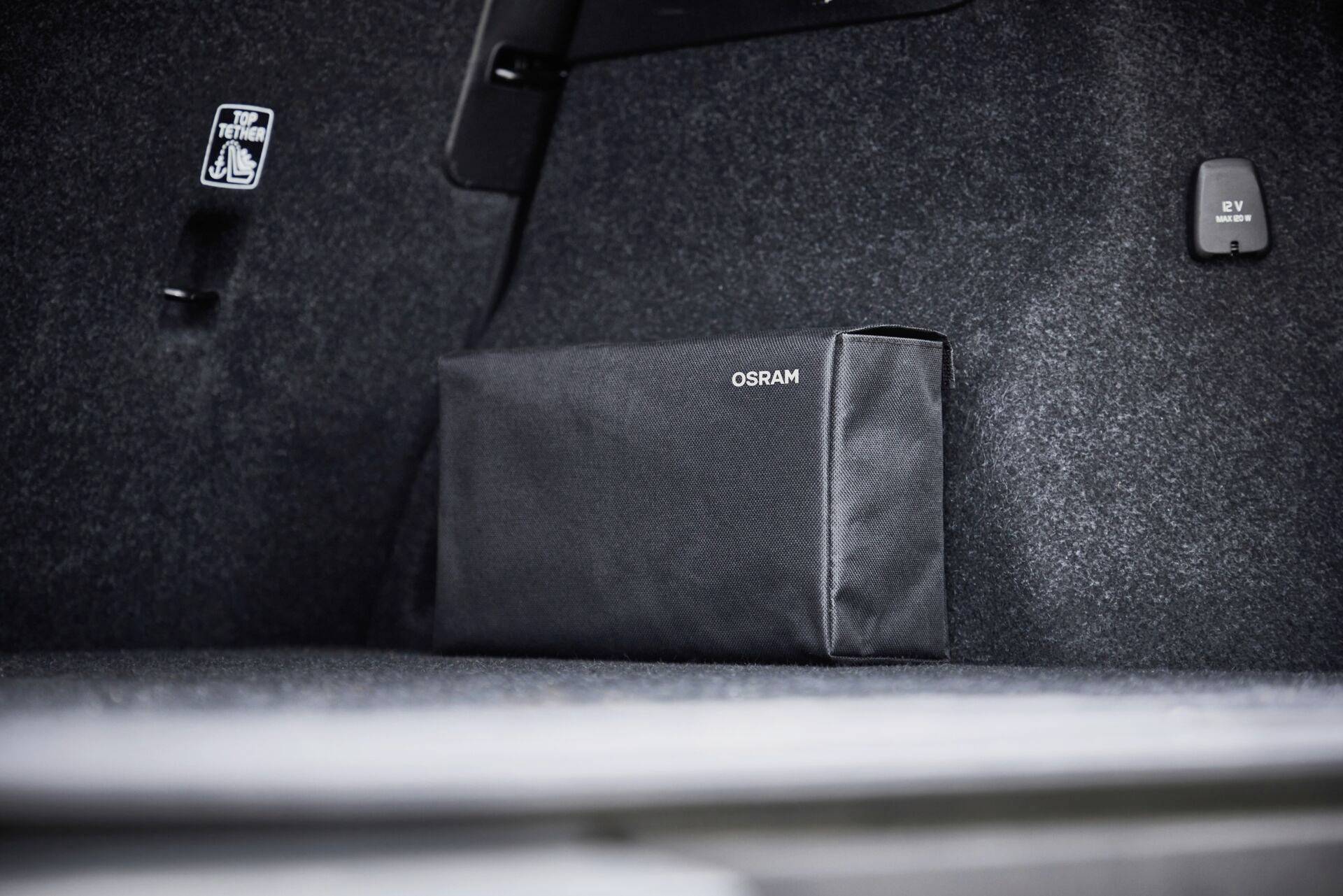 Schwarze Tasche mit 'OSRAM'-Aufschrift in einem Kofferraum; Teppichboden und Sicherheitsaufkleber sichtbar.