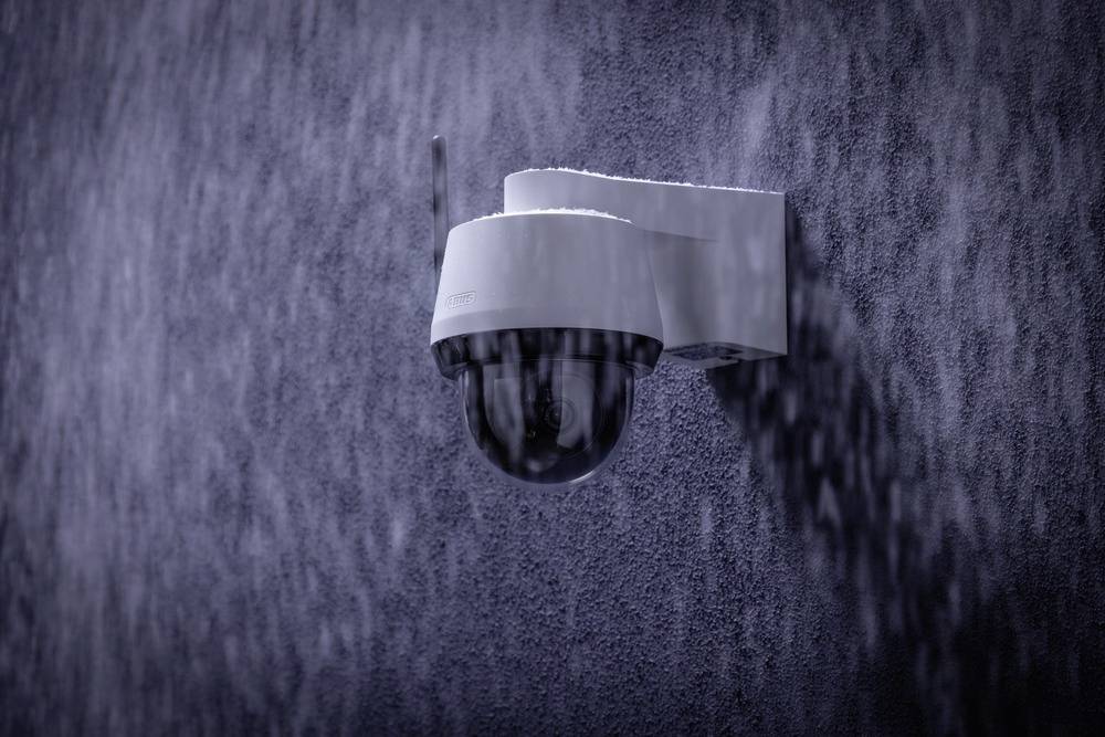 Überwachungskamera an einer Wand im Regen montiert.