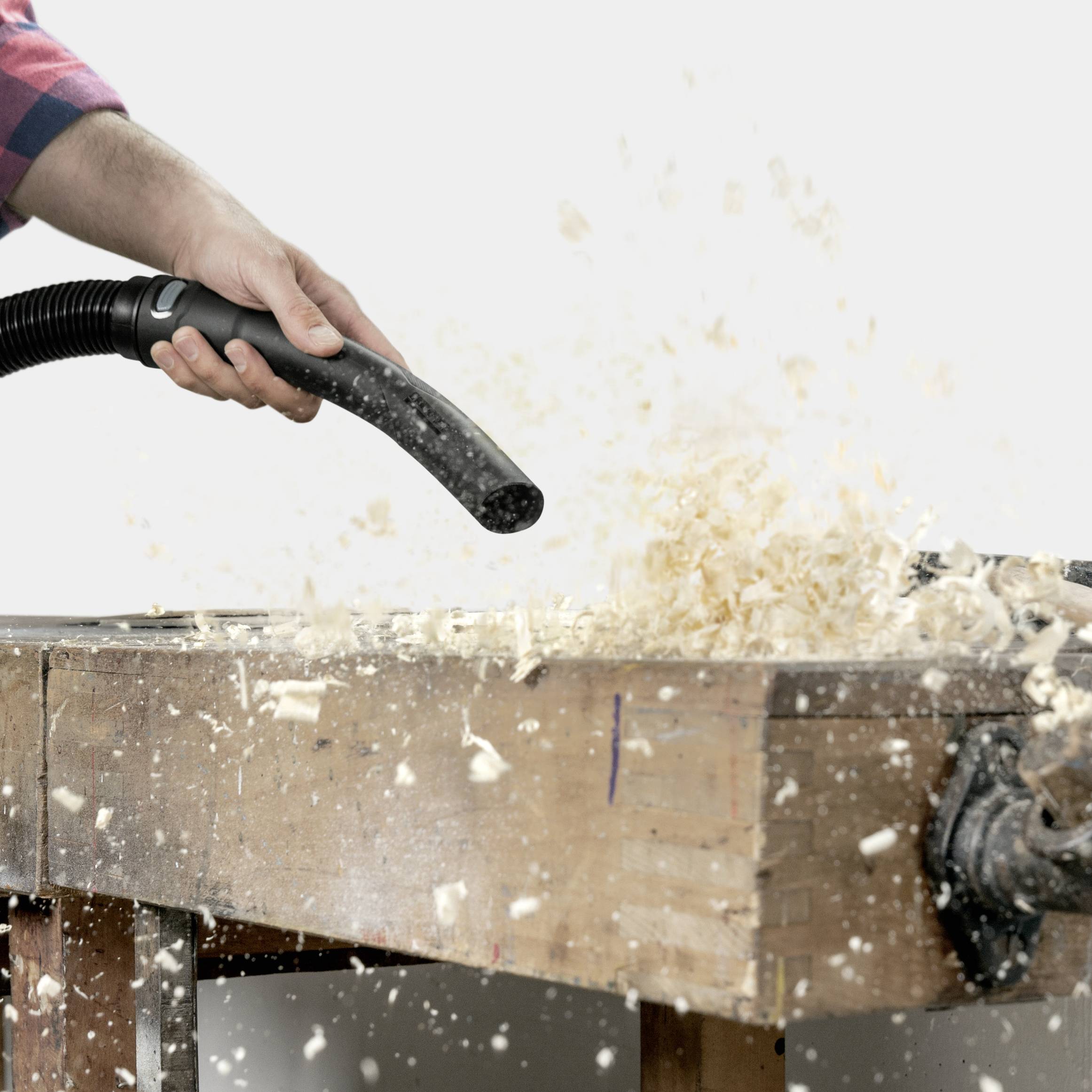 Eine Person saugt Holzspäne von einer Werkbank mit einem Staubsauger ab, deutet auf Holzarbeiten oder Tischlerei.