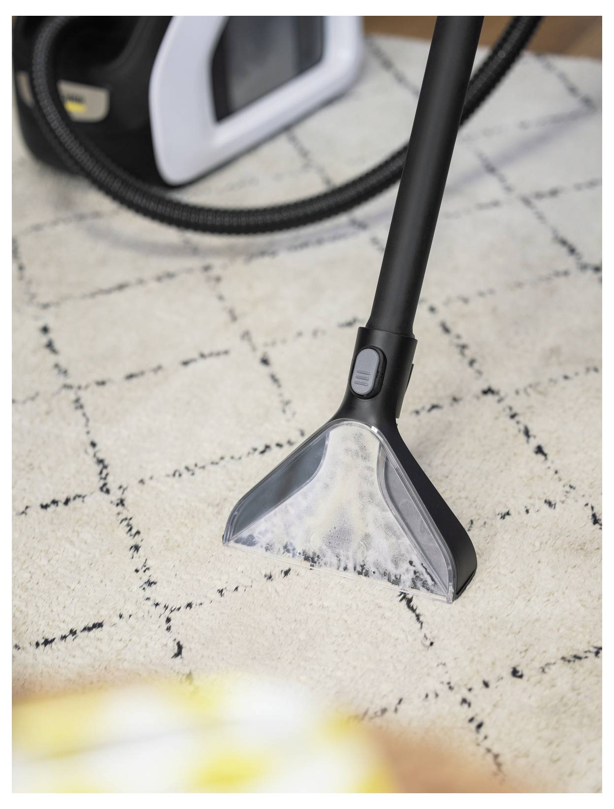 Ein Staubsaugerkopf auf einem hellgefärbten Teppich. Der Staubsauger scheint in Gebrauch zu sein, wobei der Saugkopf sichtbar die Teppichoberfläche reinigt.