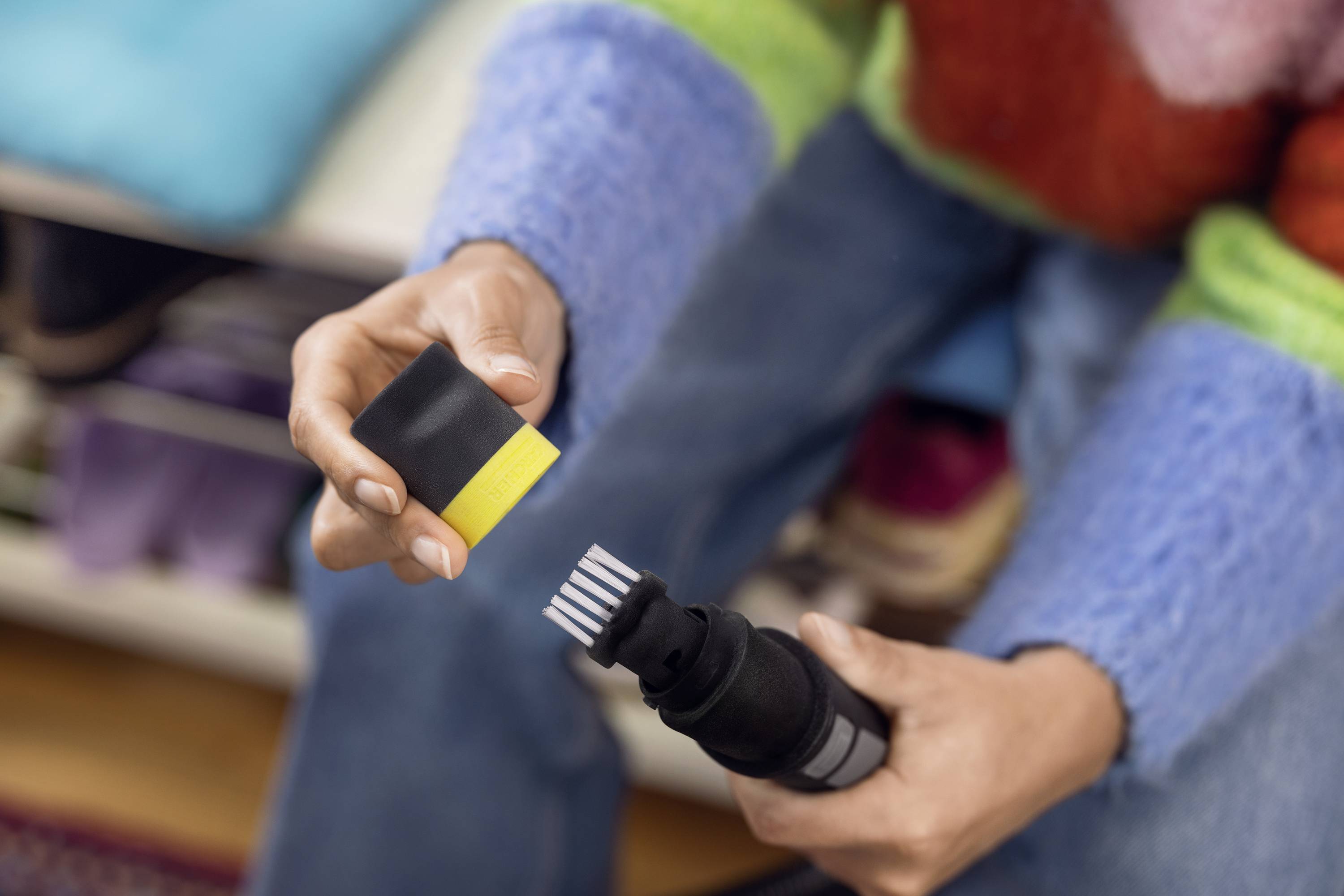 Eine Person hält ein Autoladegerät in der Hand, während sie den Stecker inspiziert. Im Hintergrund sind bunte Kleidungsstücke zu sehen.