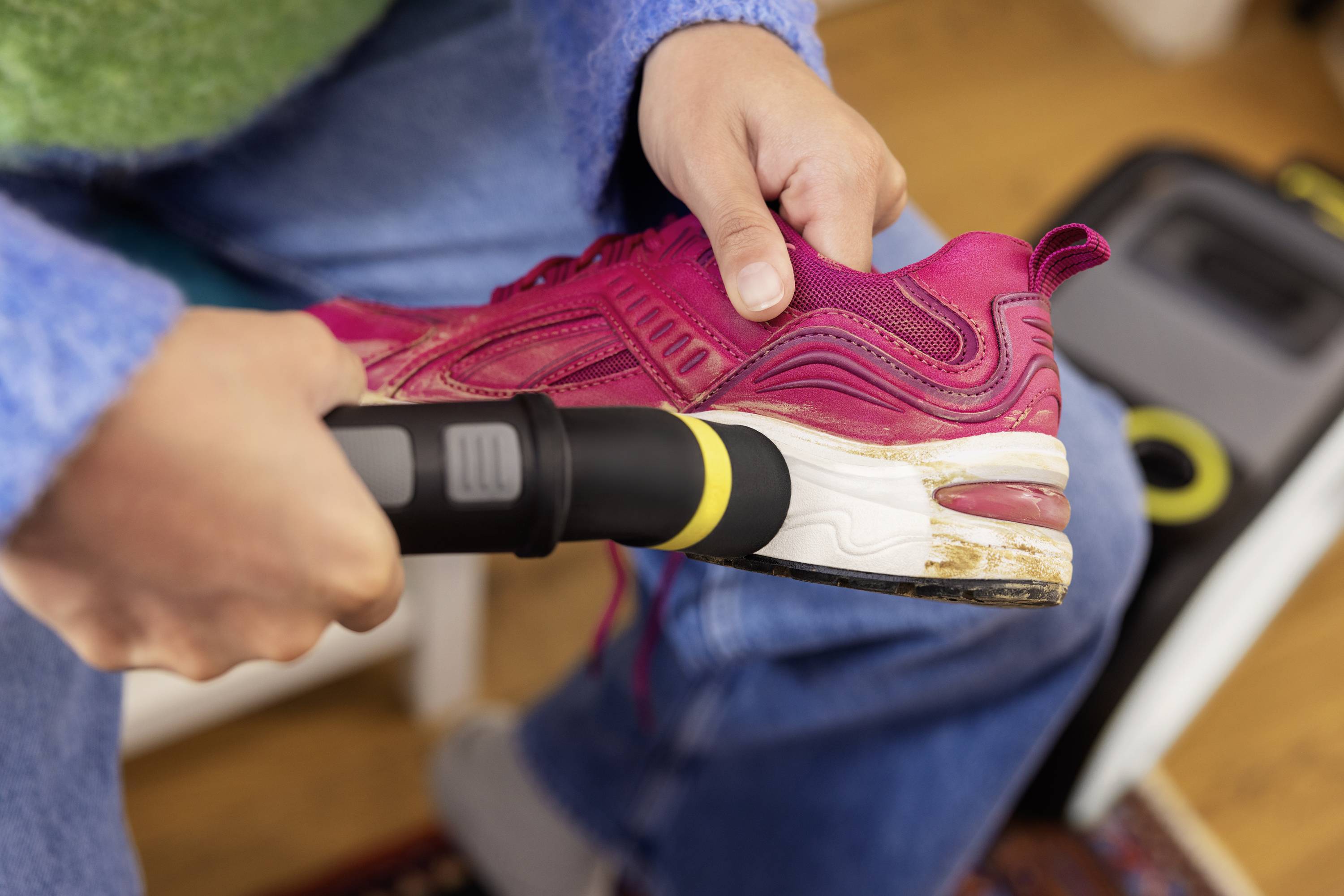 Person reinigt einen roten Sportschuh mit einem Staubsauger. Der Fokus liegt auf der Sohle des Schuhs, der in einer Hand gehalten wird.
