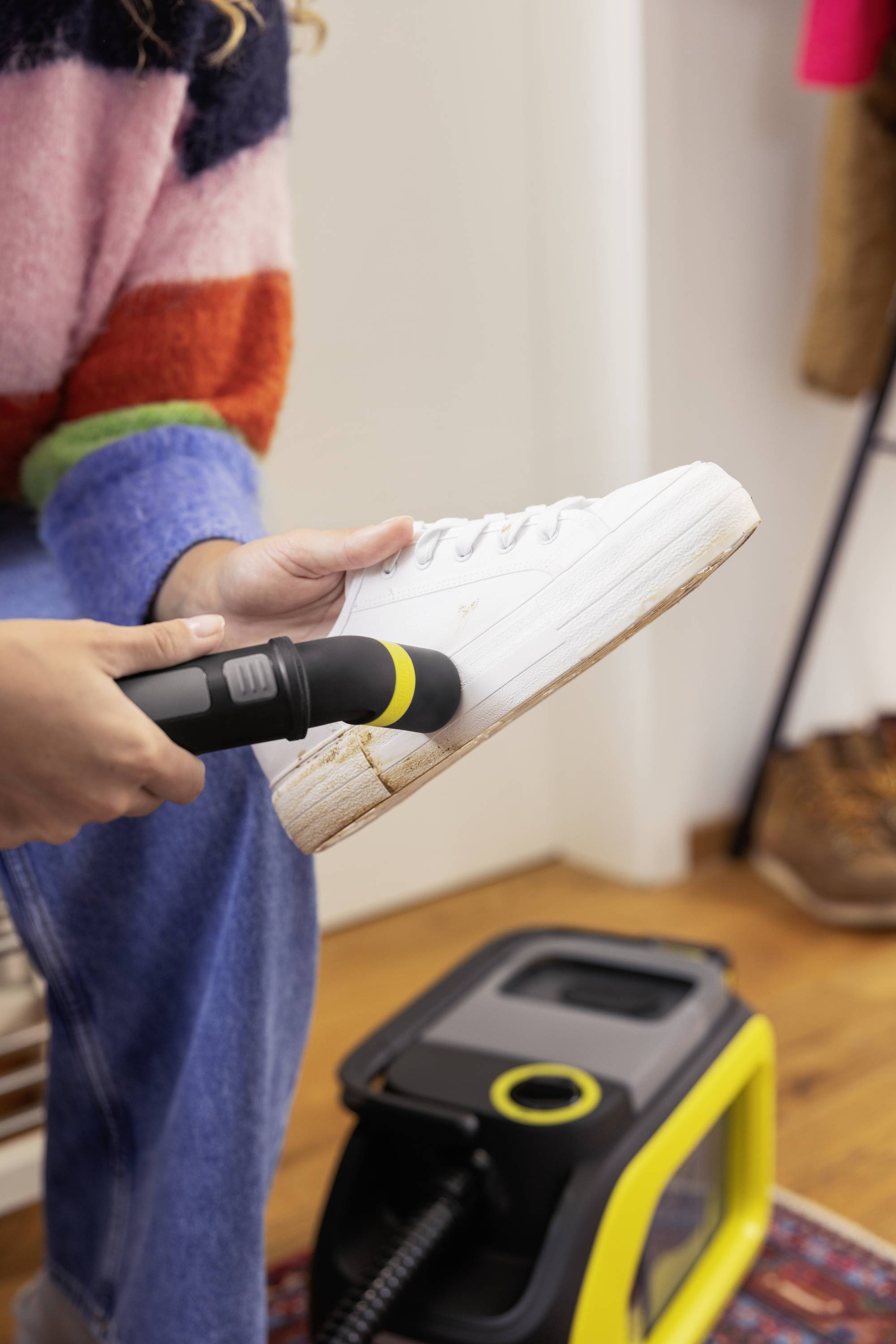 Person reinigt weißen Sneaker mit einer kleinen Bürste und einem Dampfreiniger. Der Sneaker hat sichtbare Schmutzflecken.