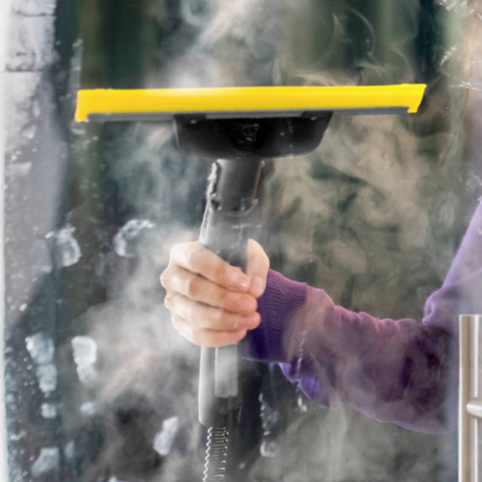 Eine Person, die einen Dampfreiniger verwendet, um Flecken zu entfernen oder eine Oberfläche zu reinigen. Das Gerät emittiert sichtbaren Dampf, der auf eine aktive Reinigung hinweist.