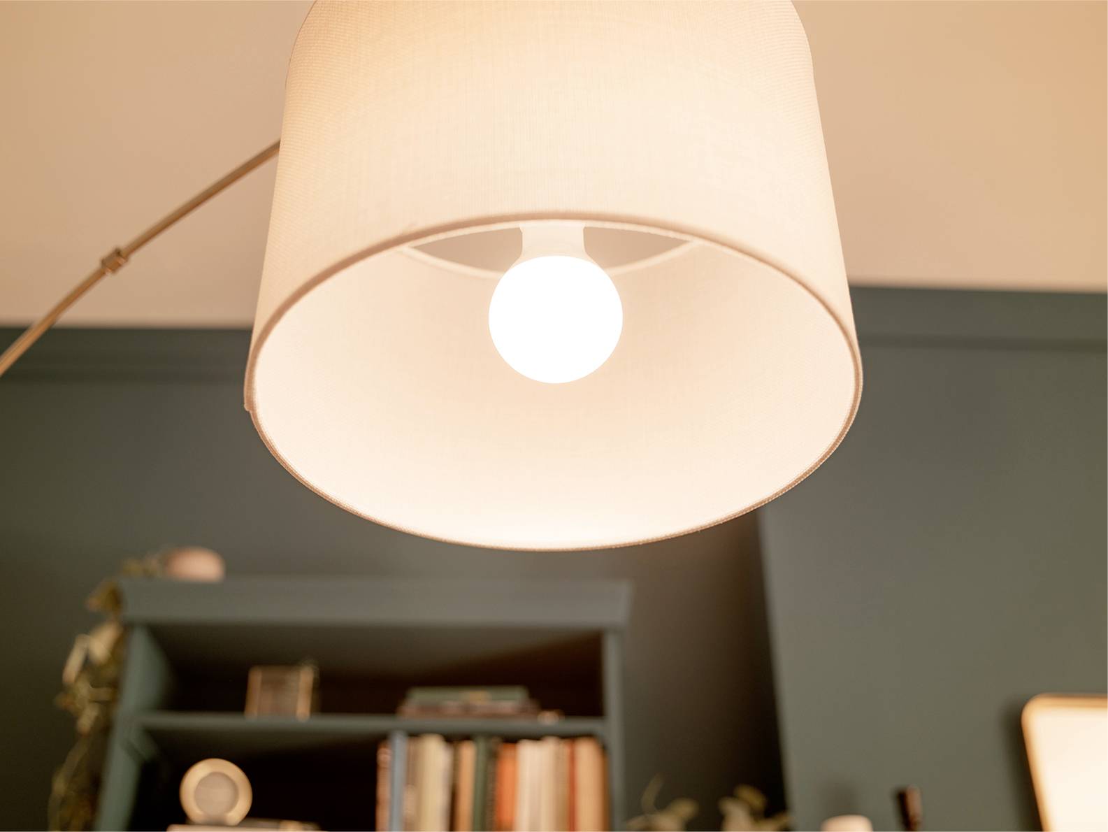 Eine eingeschaltete Glühlampe in einer Stehlampe beleuchtet ein Wohnzimmer mit einem Bücherregal im Hintergrund.