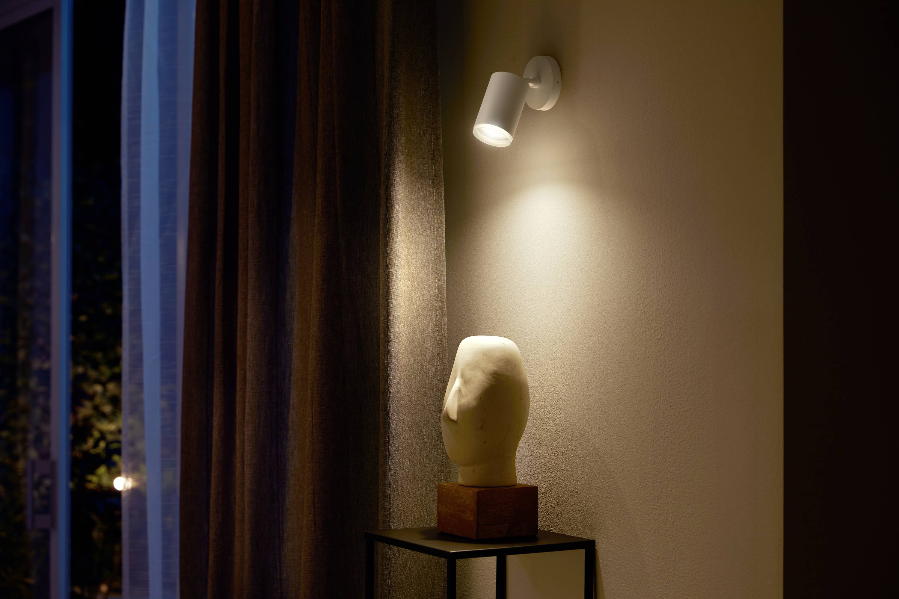 Ein beleuchteter Raum mit einem weißen Kunstkopf auf einem schwarzen Sockel, angestrahlt von einem Spotlicht. Im Hintergrund sind Vorhänge zu sehen.