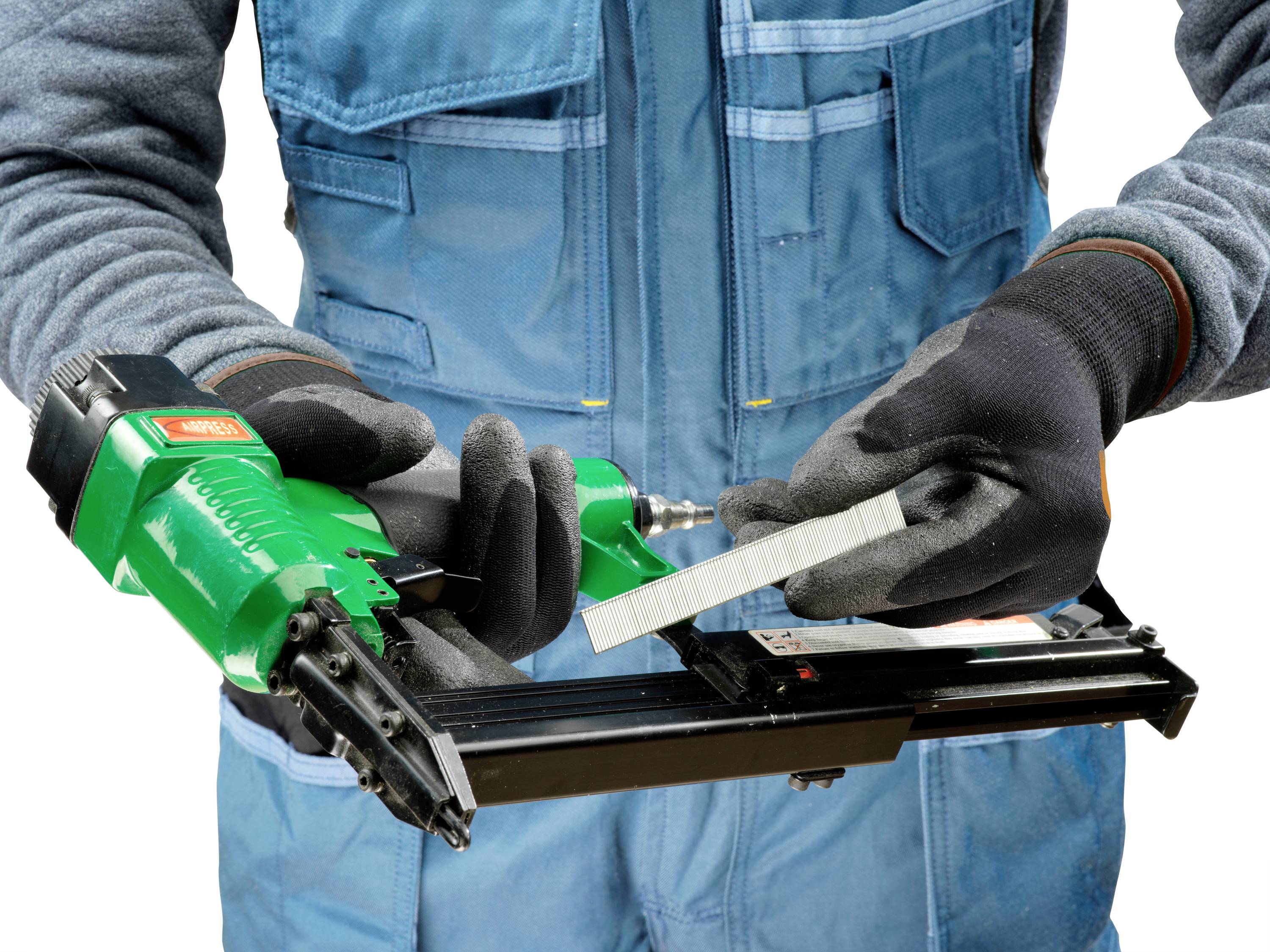 Ein Arbeiter in blauer Arbeitskleidung und schwarzen Handschuhen hält einen grünen Druckluftnagler und eine Reihe von Nägeln.