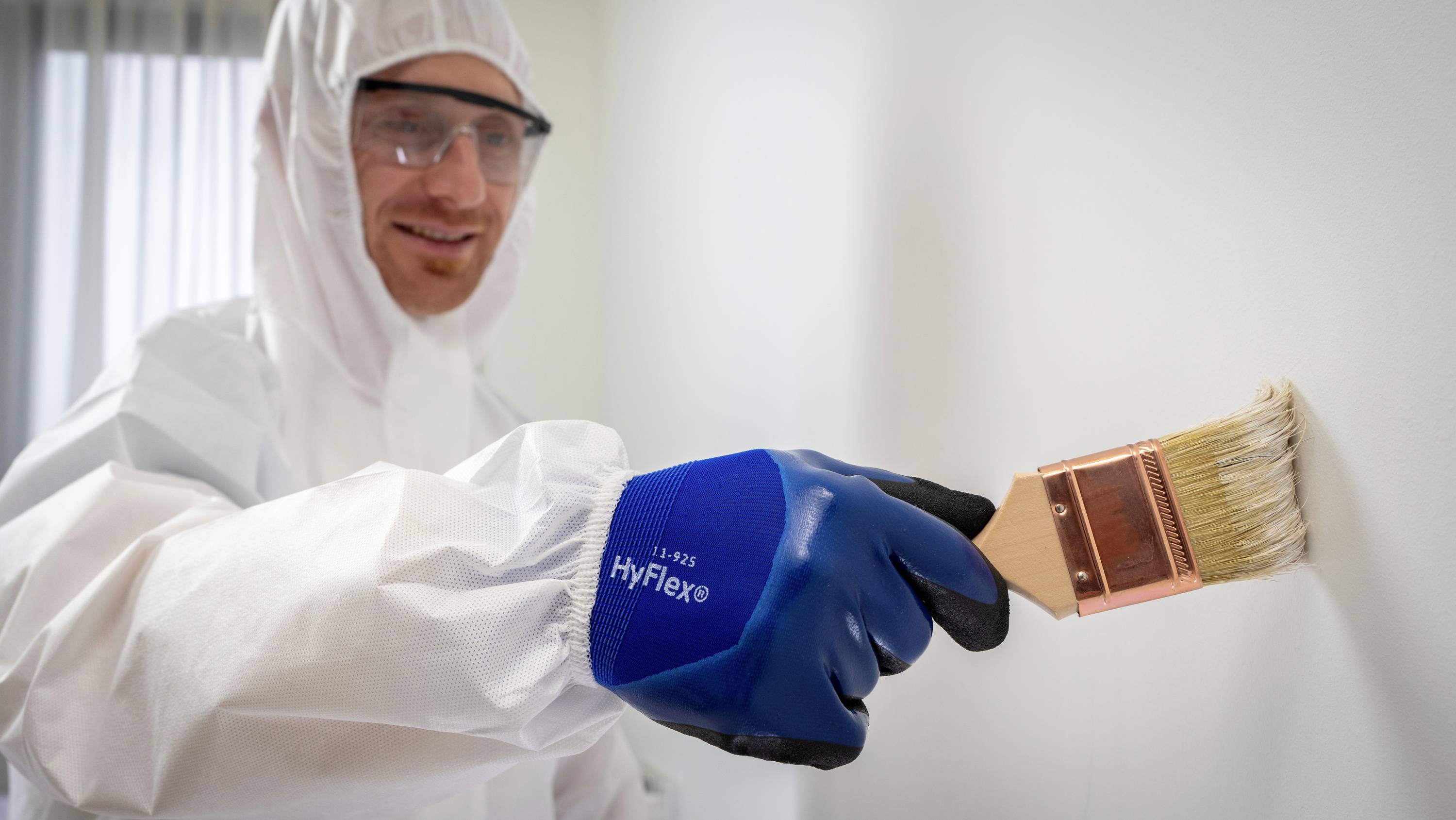 Eine Person in Schutzkleidung streicht eine Wand mit einem Pinsel.