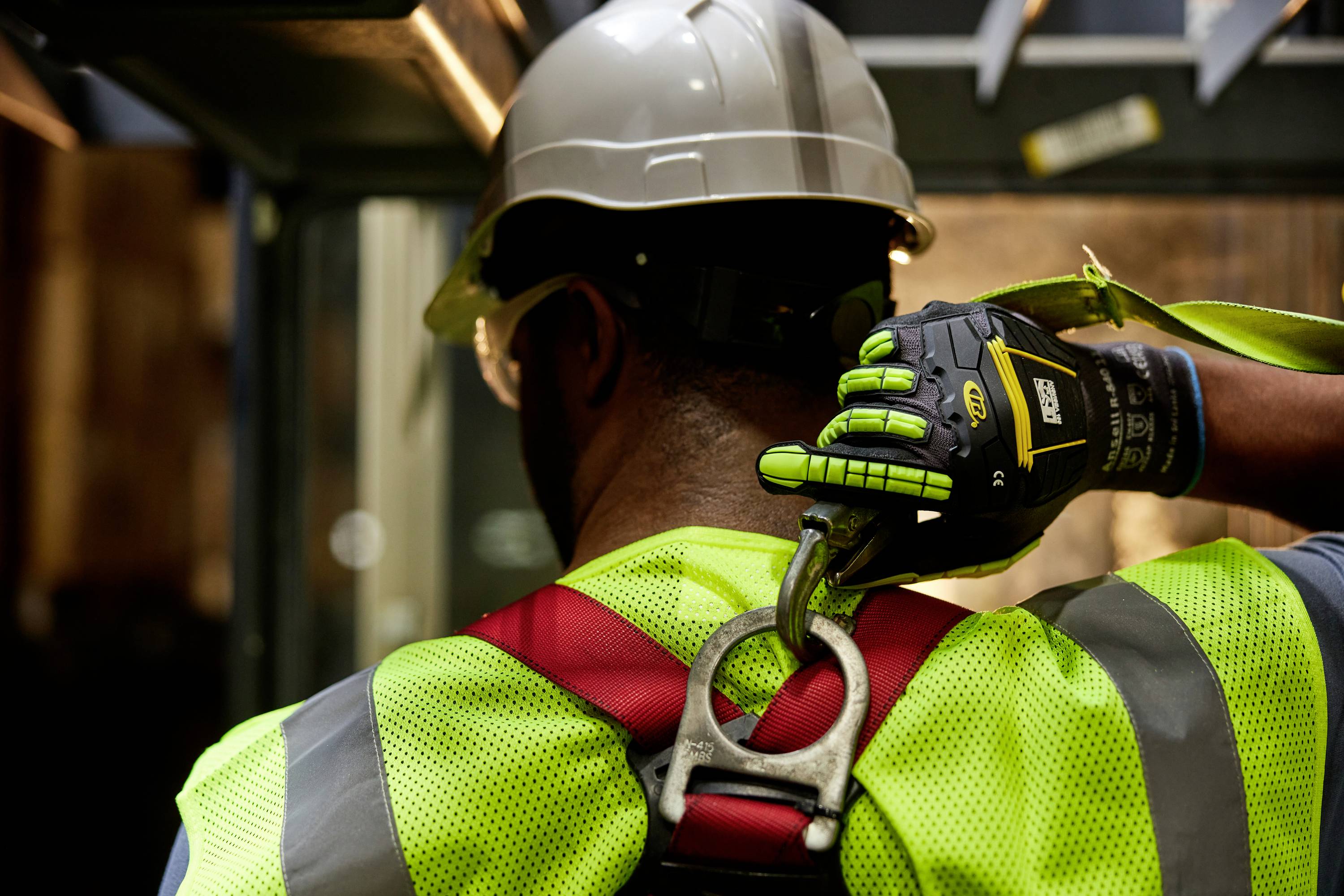 Eine Person trägt Schutzkleidung und einen Helm, während sie im Bau arbeitet. Sie befestigt einen Sicherheitsgurt an einem Ankerpunkt.