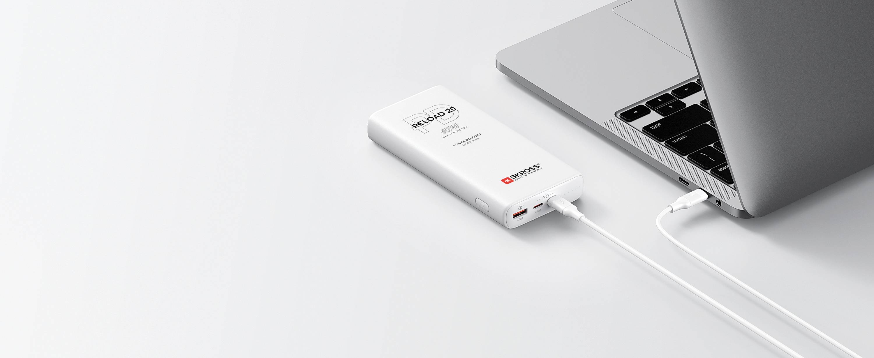 Eine Powerbank ist über ein USB-Kabel mit einem Laptop verbunden, der auf einem weißen Tisch liegt.