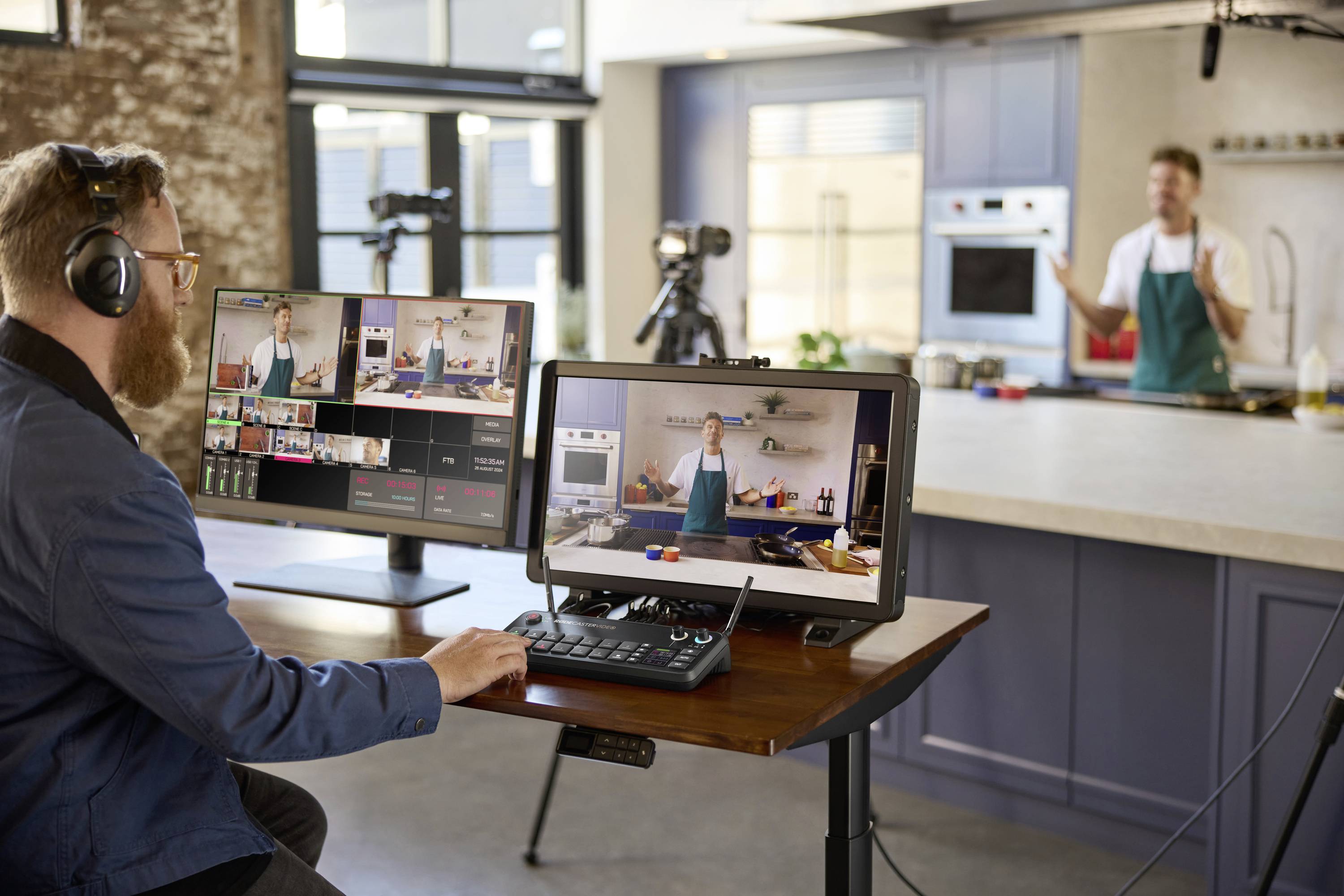 Ein Mann mit Kopfhörern sitzt an einem Schreibtisch mit Computern und Videotechnik, während ein Koch im Hintergrund filmt.