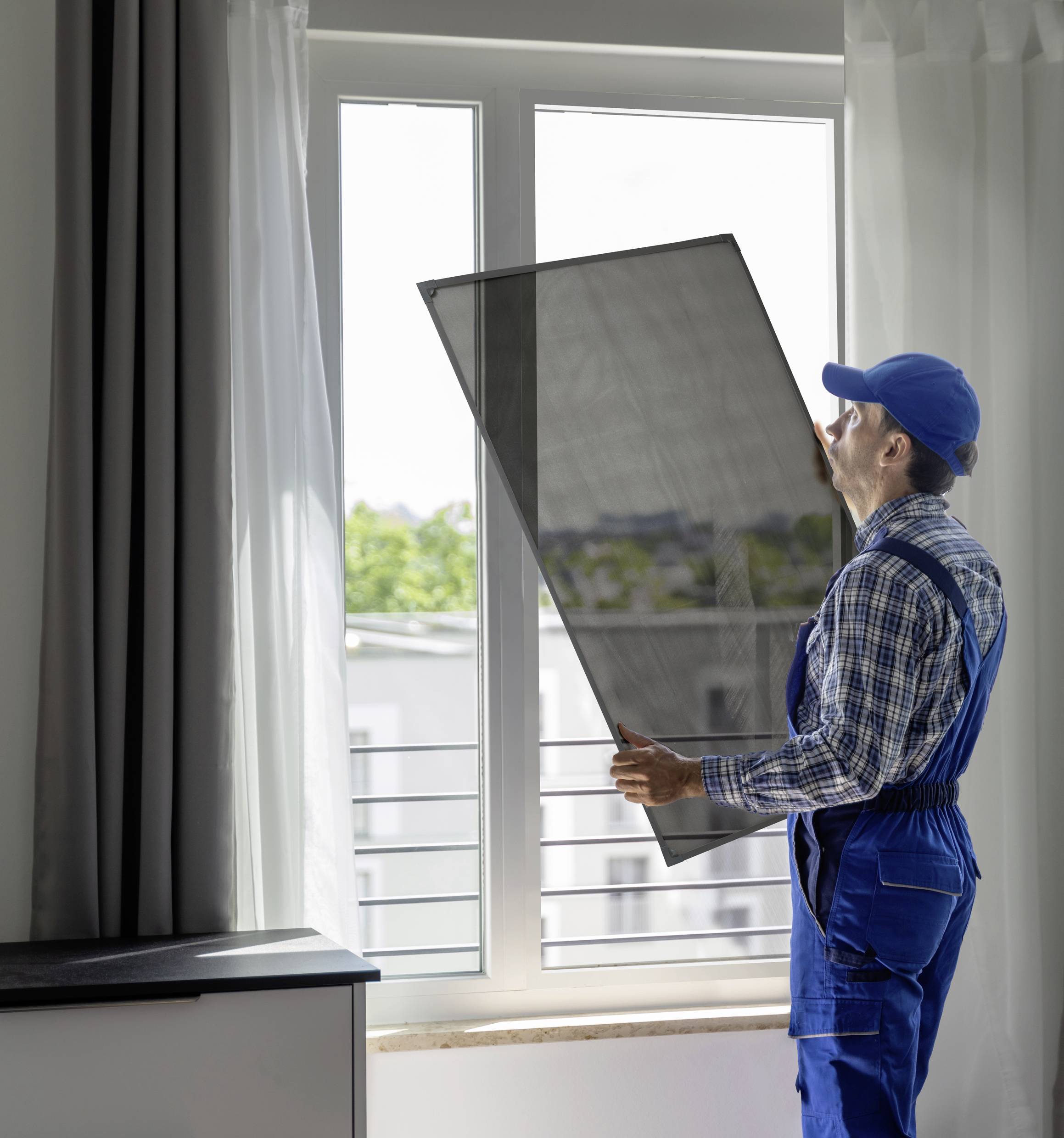 Ein Arbeiter im blauen Overall montiert eine Fensterscheibe in einem modernen Raum mit weißen Vorhängen.