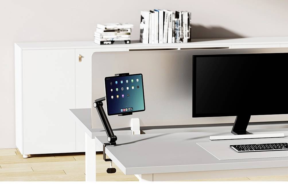 Ein moderner Arbeitsplatz mit einem großen Monitor, einer Tastatur und einem Tablet auf einem Halterarm, Bücherregal im Hintergrund.