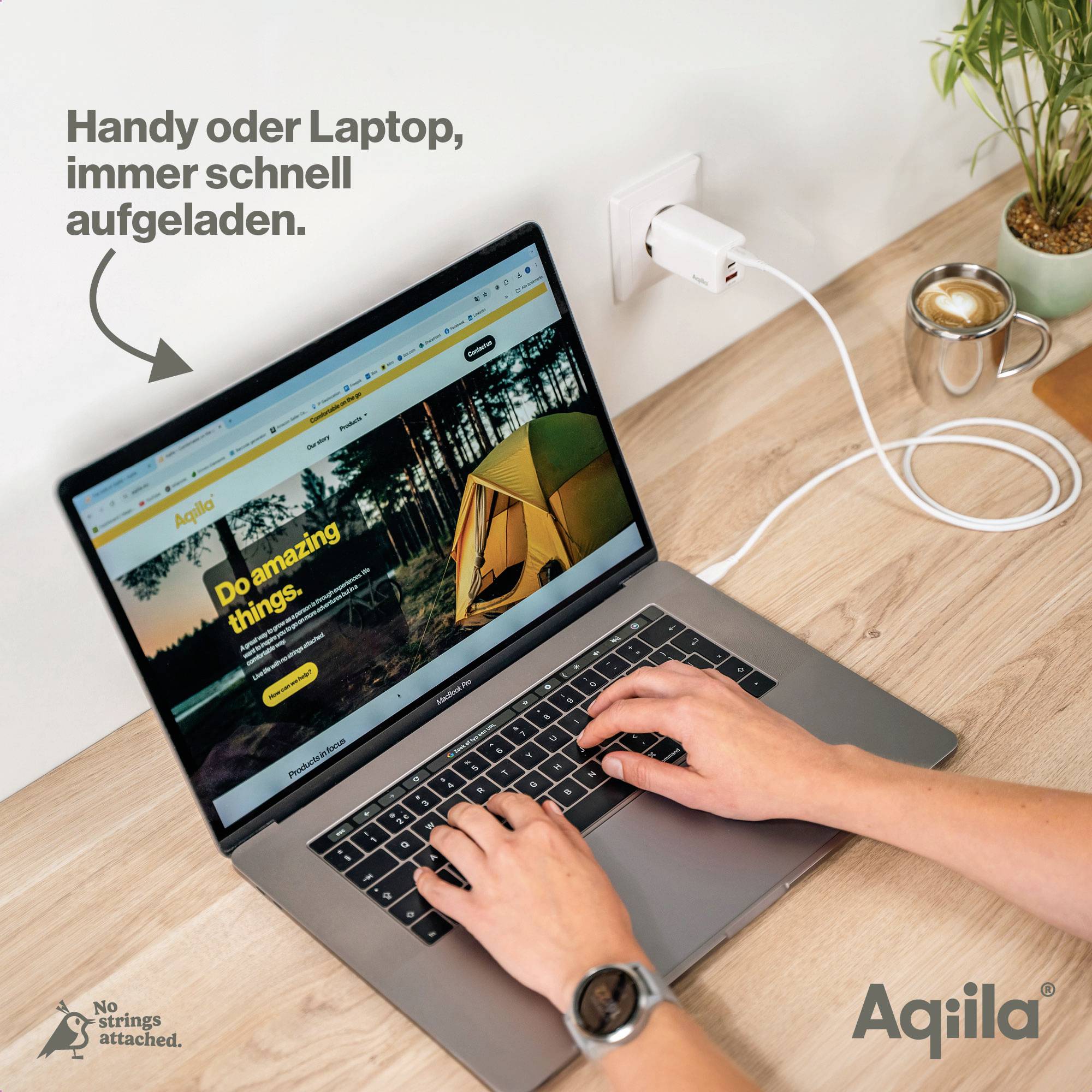 Eine Person lädt einen Laptop an einer Wandsteckdose auf. Auf dem Bildschirm steht 'Do amazing things'. Ein Handy liegt daneben.