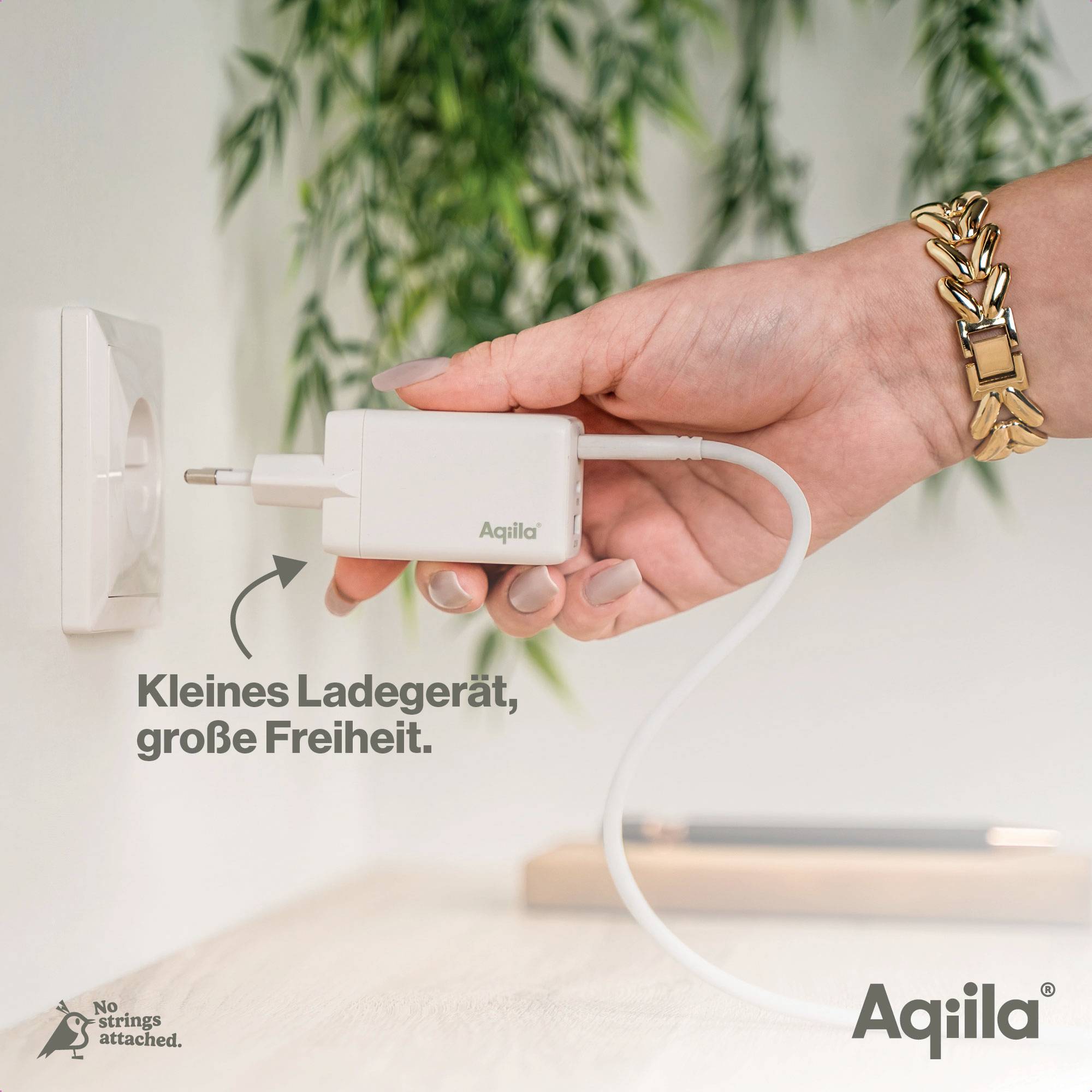 Eine Hand steckt ein Ladegerät der Marke 'Aqila' in eine Steckdose. Text: 'Kleines Ladegerät, große Freiheit'.
