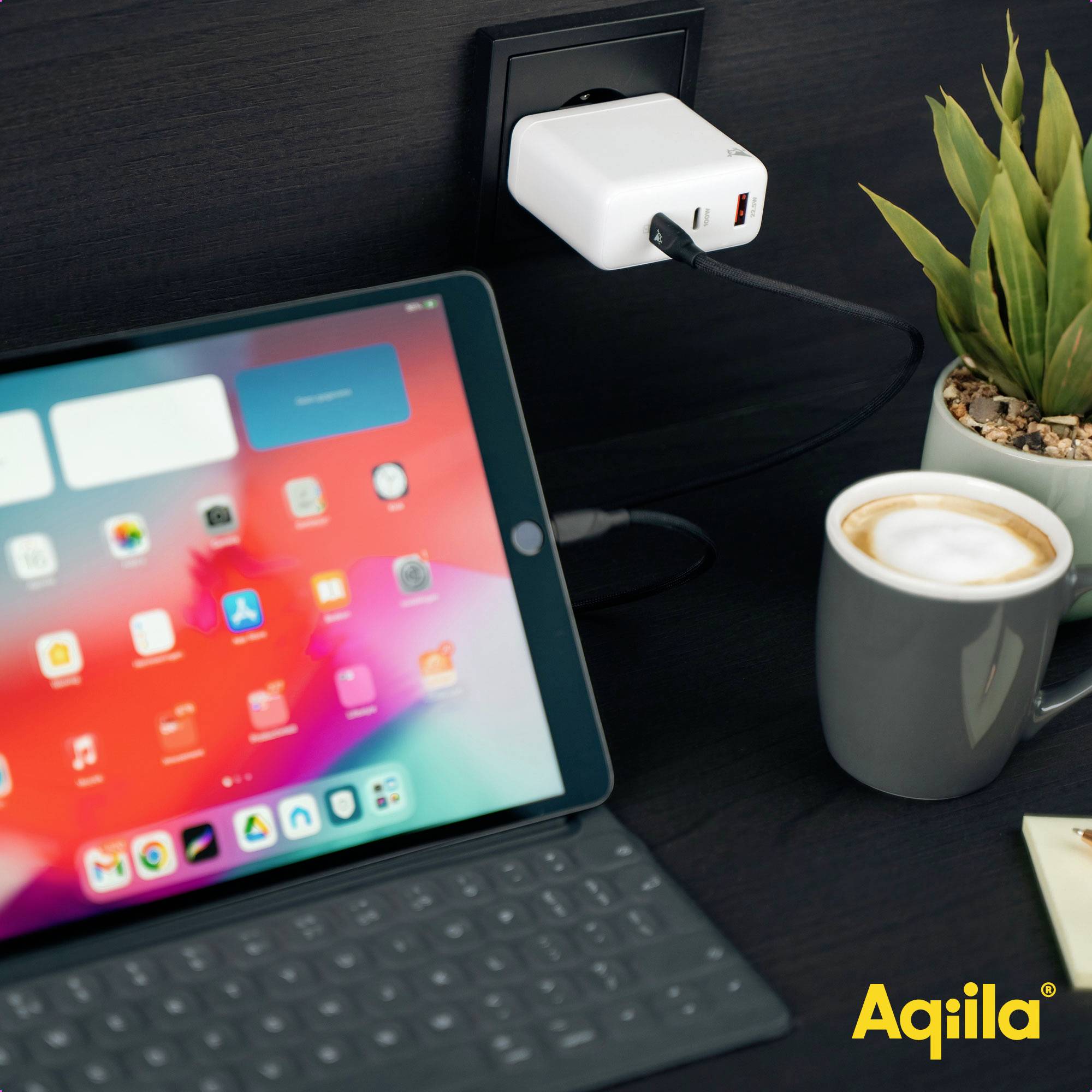 Ein Tablet ist an eine Steckdose angeschlossen. Daneben stehen eine Tasse Kaffee und eine Pflanze. Das Logo 'Aqila' ist unten rechts.