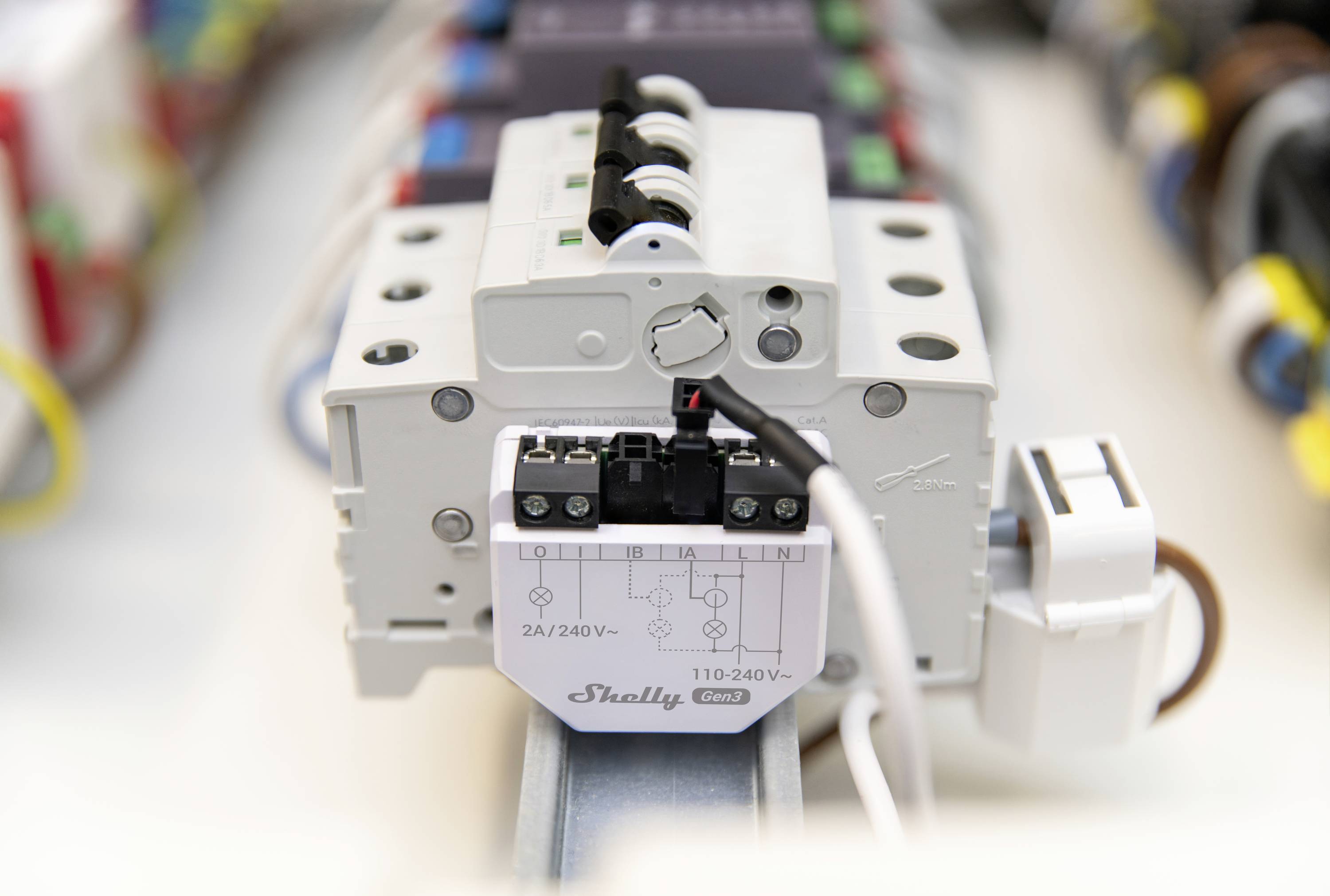 Ein elektrisches Relais mit Beschriftung 'Shelly 2.4/240V' ist auf einer DIN-Schiene montiert, umgeben von farbigen Kabeln.