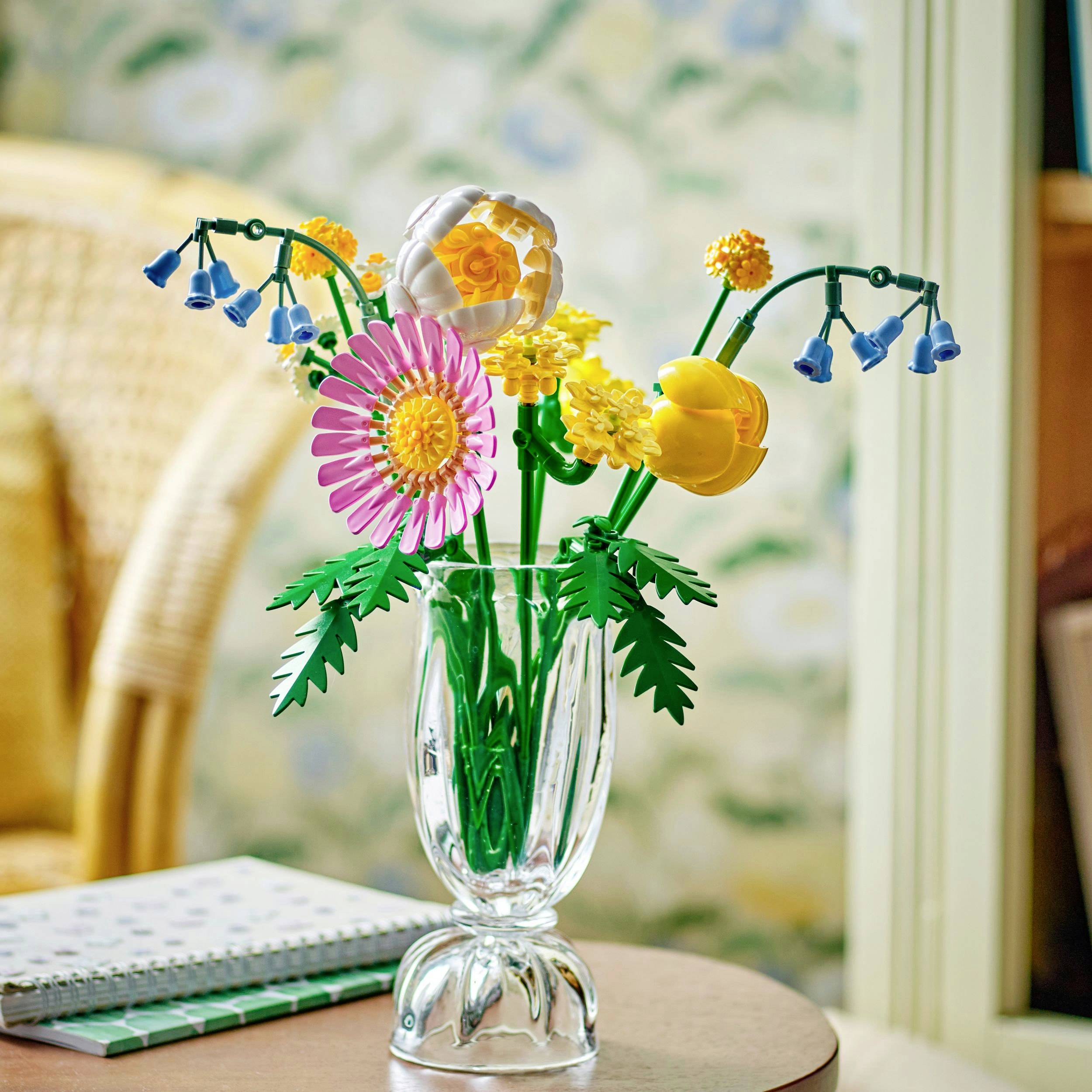 Ein glasartige Vase steht auf einem Tisch und enthält detailreich gestaltete Blumen aus Bausteinen in verschiedenen Farben und Formen.